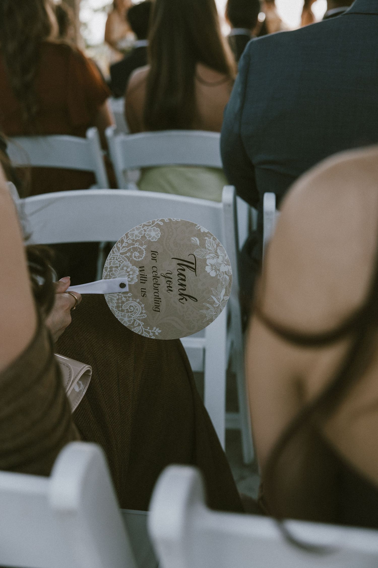 Wedding guest holding decorative round fan with thank you message during outdoor ceremony.