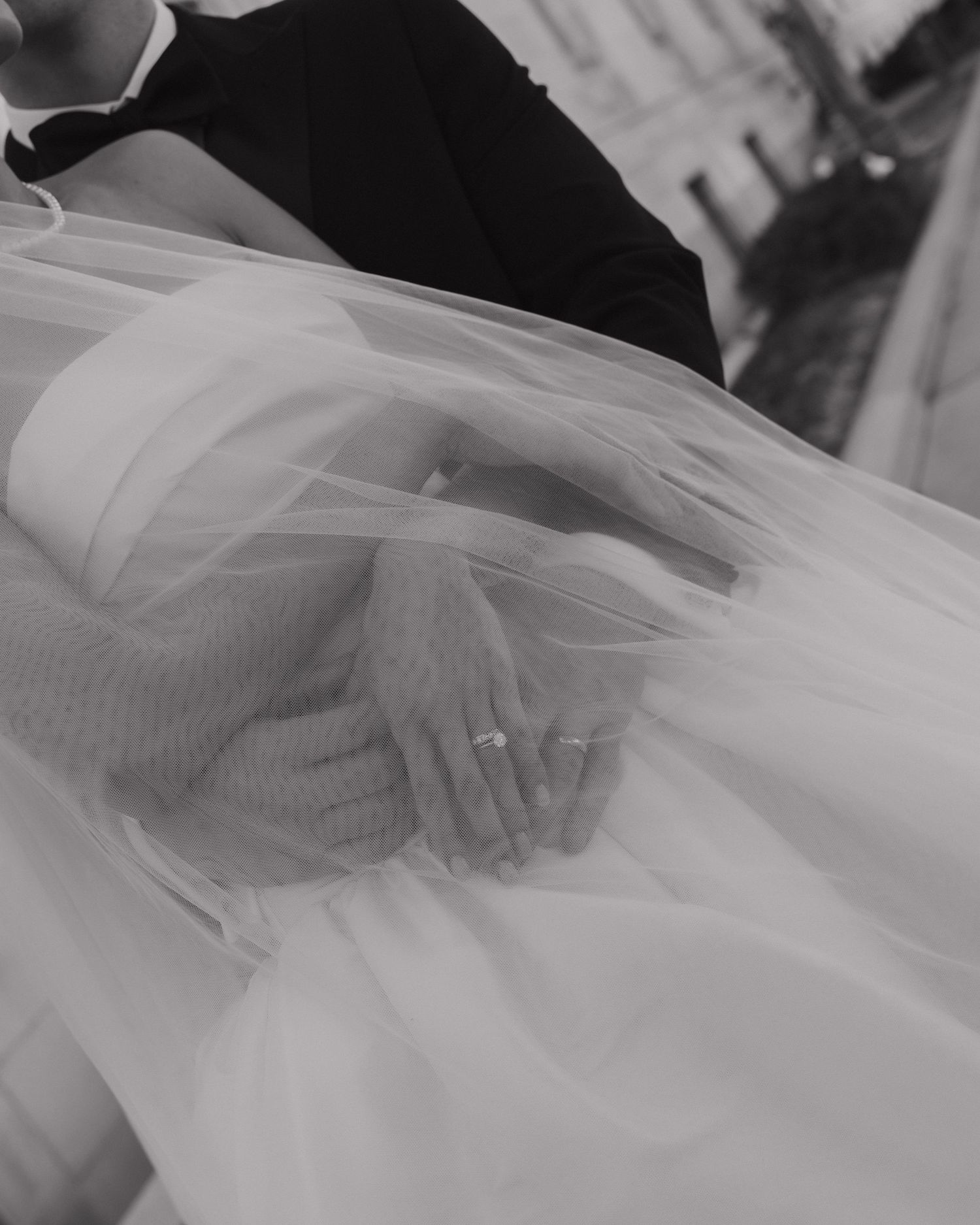 Close-up of bride and groom holding hands through sheer wedding veil in black and white.