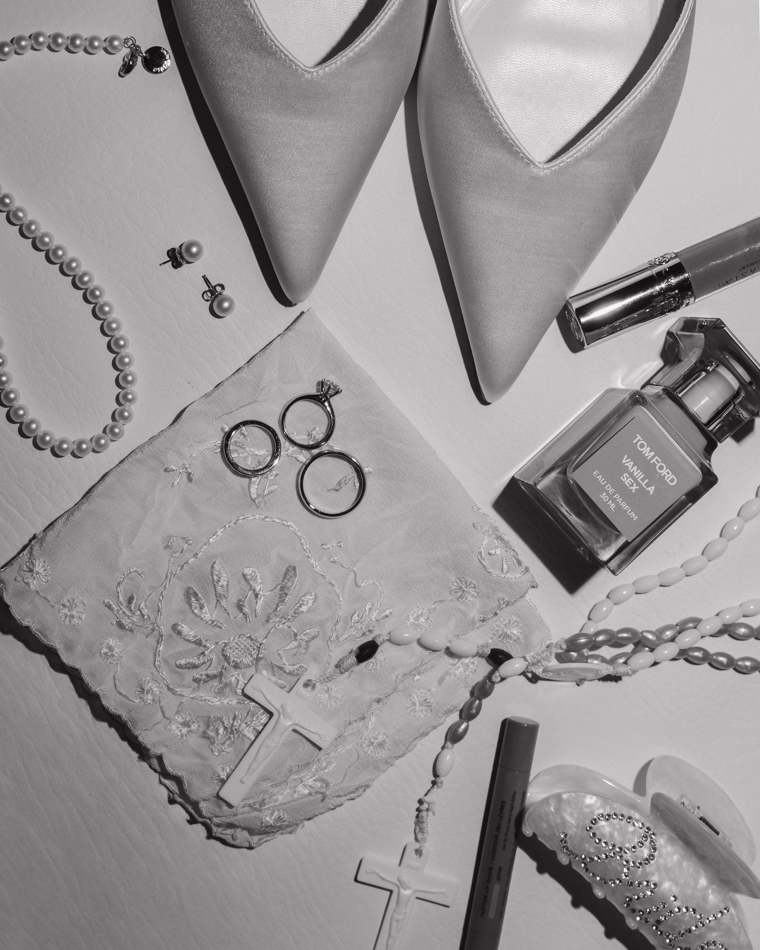 Flat lay of bridal accessories including pearl necklace, rings, heels, perfume, and lace garter.