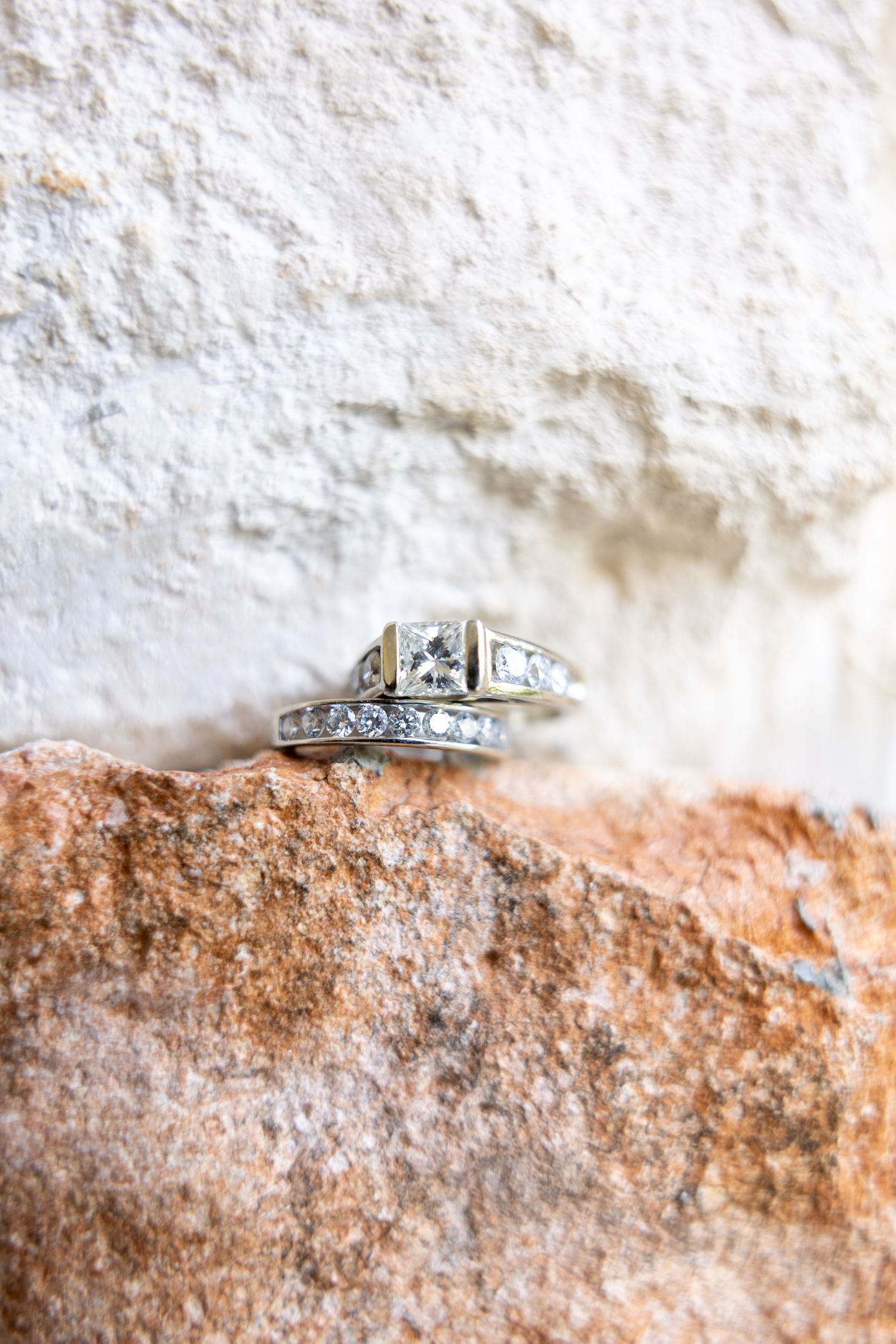 Diamond engagement ring and wedding band displayed on a rustic stone surface.
