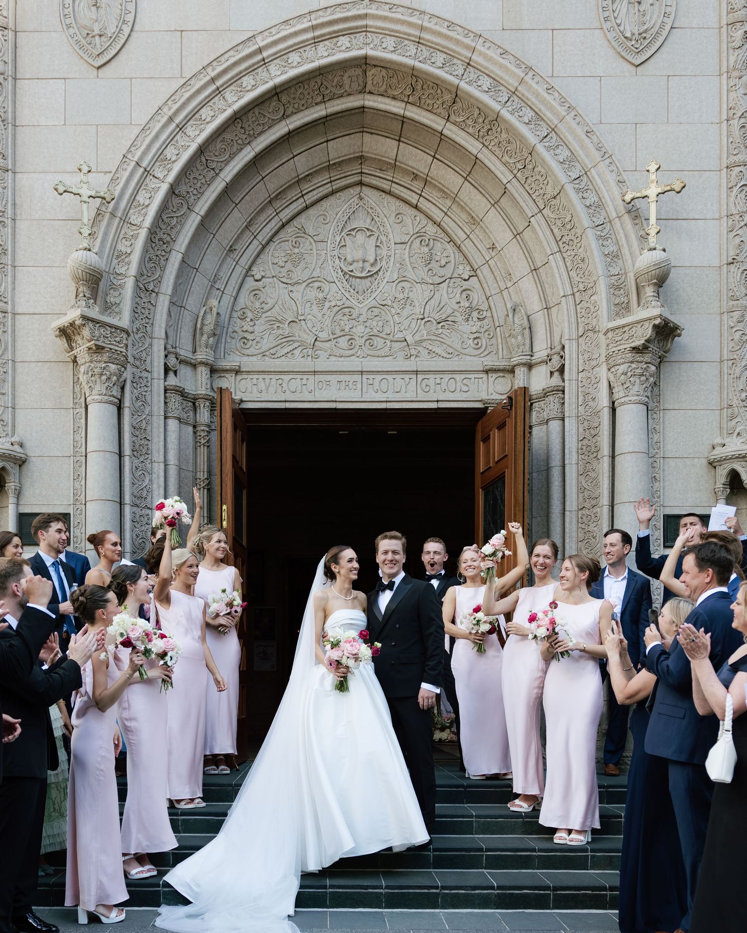 Wedding party celebrates outside ornate church entrance with bridesmaids in blush pink dresses.