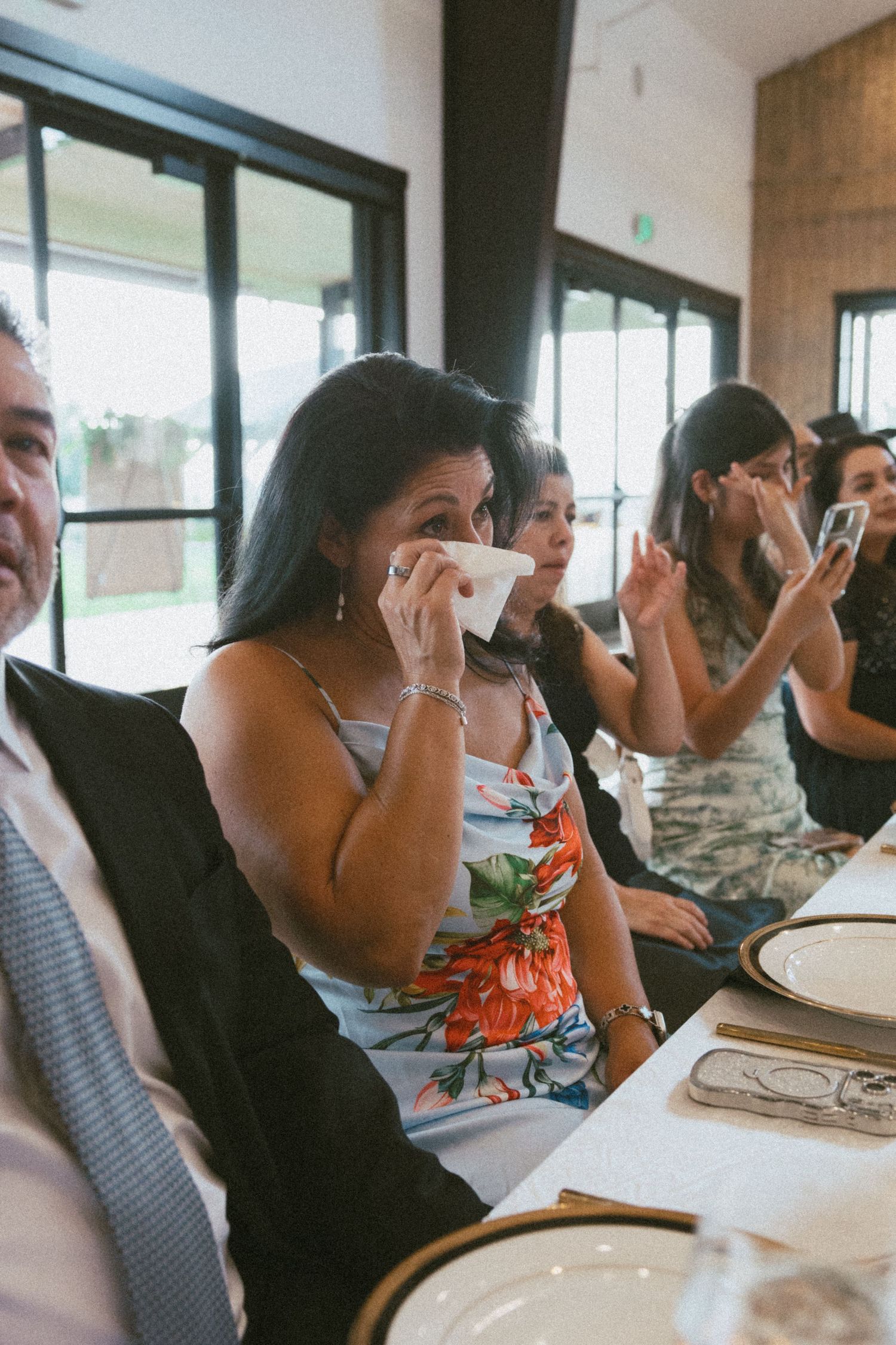 Emotional wedding guest wiping tears during heartfelt reception speech at elegant dinner.
