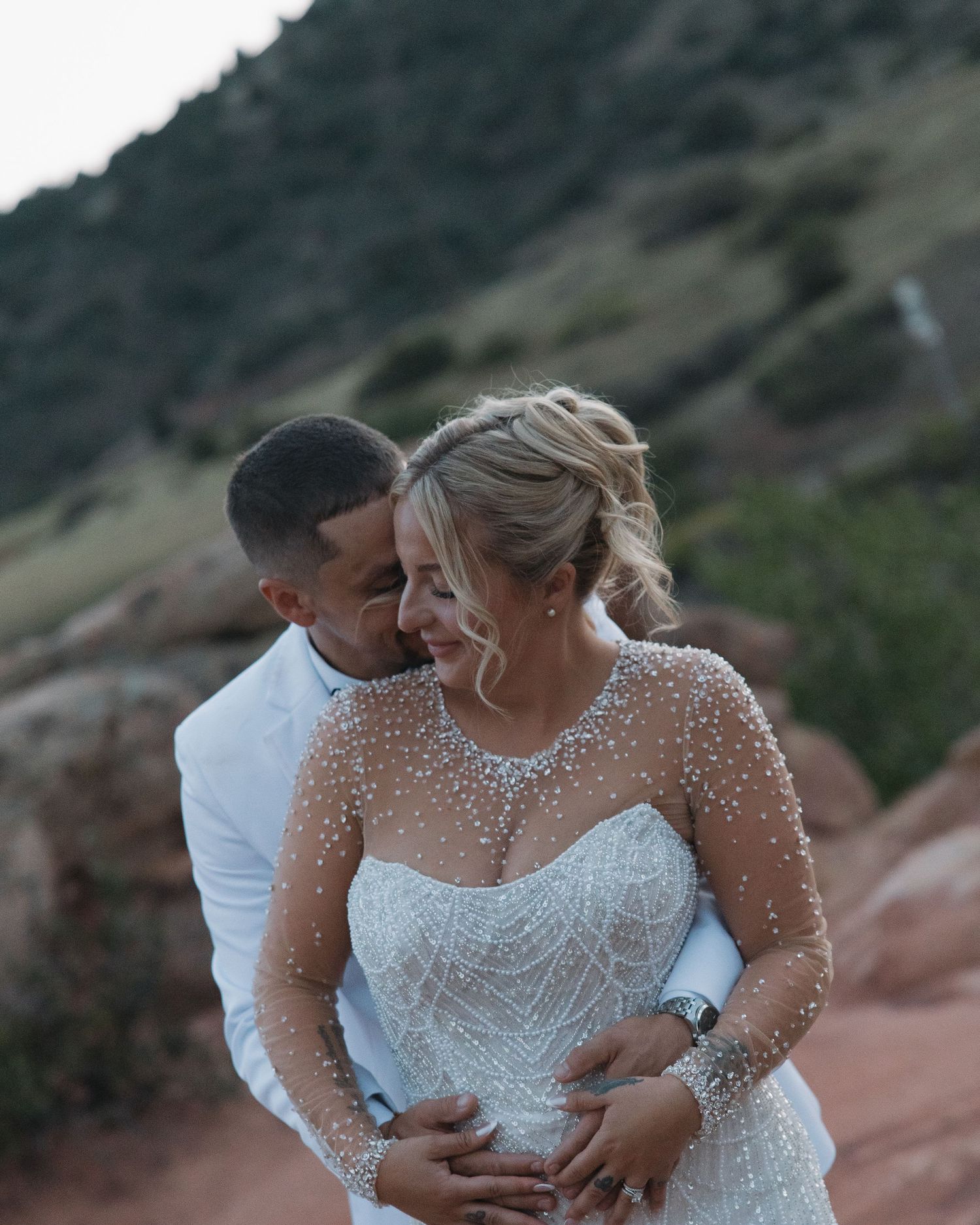 Bride and groom embracing outdoors at red rocks, bride wearing beaded long sleeve wedding gown.