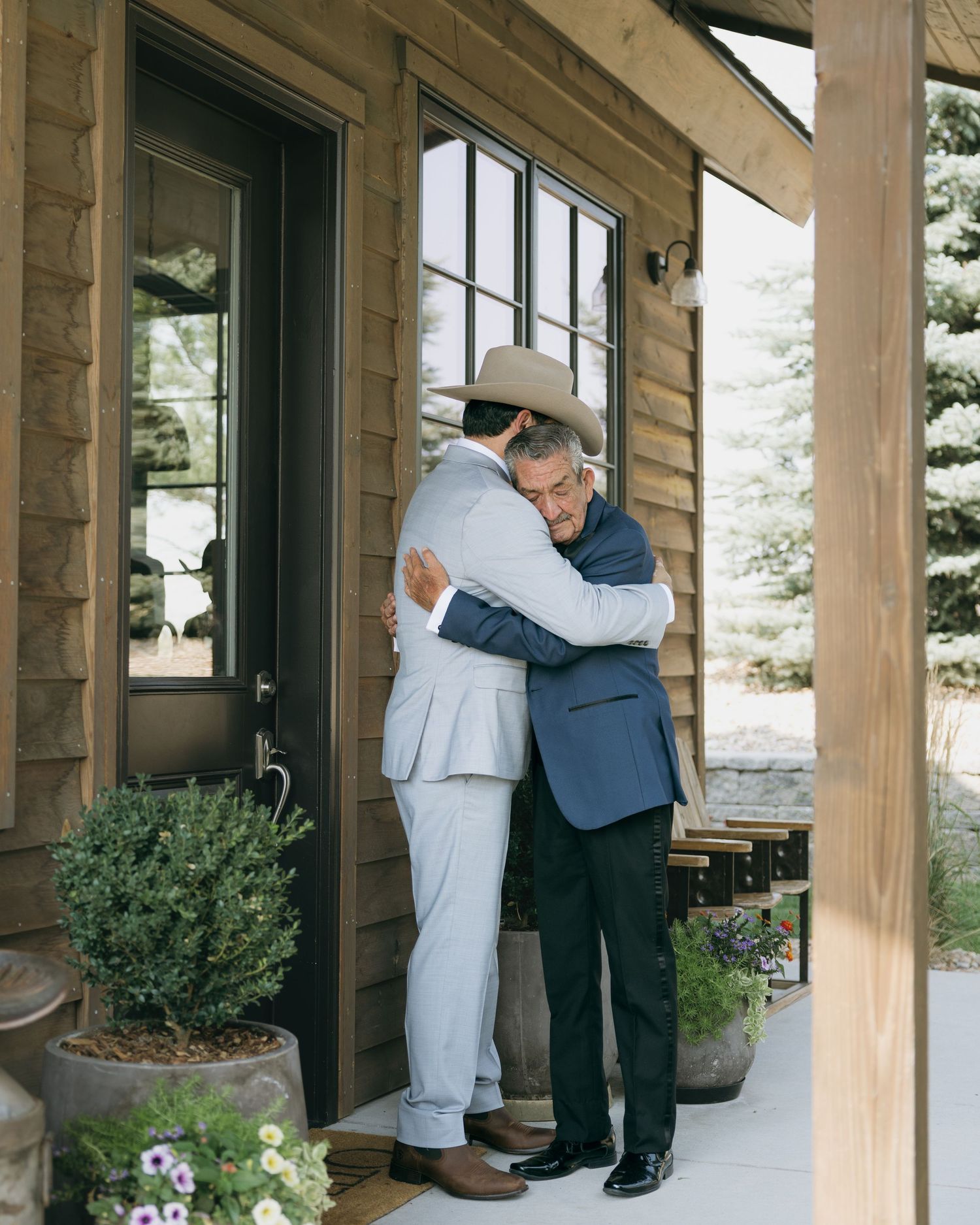 Two men sharing an emotional hug on rustic wooden porch during wedding celebration.