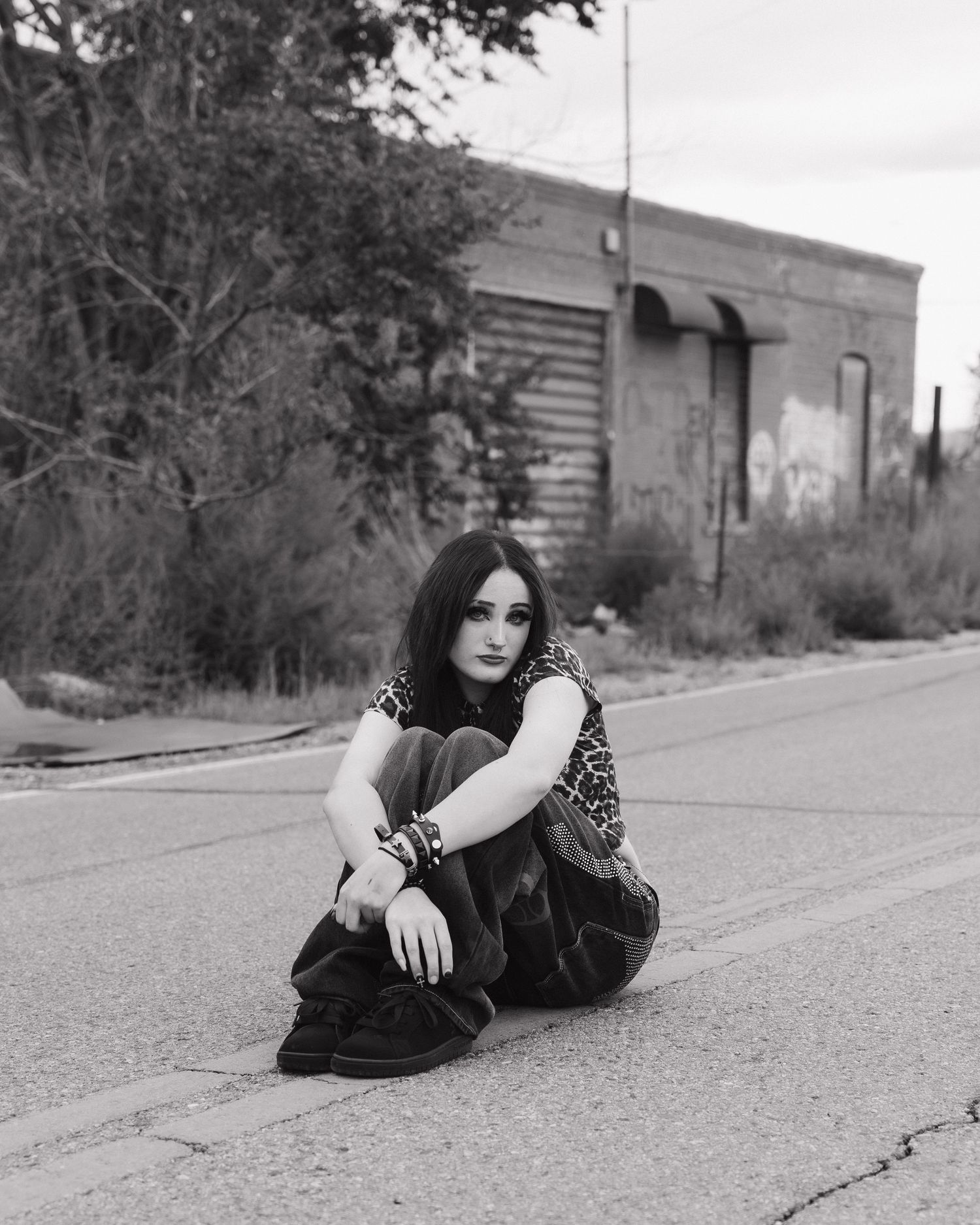 Black and white portrait of young woman sitting on street in front of urban building.