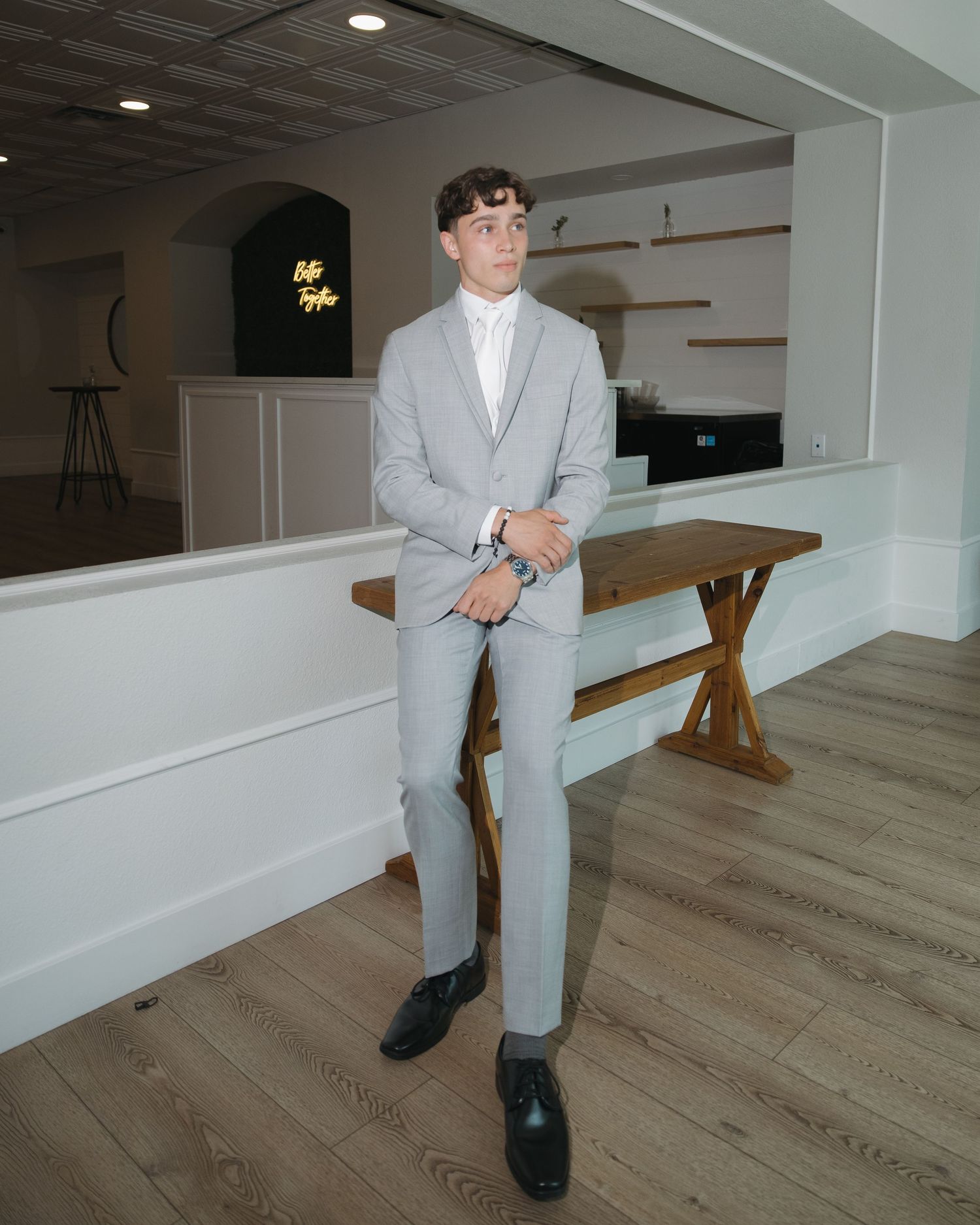 Young man in gray suit poses confidently in modern venue interior.