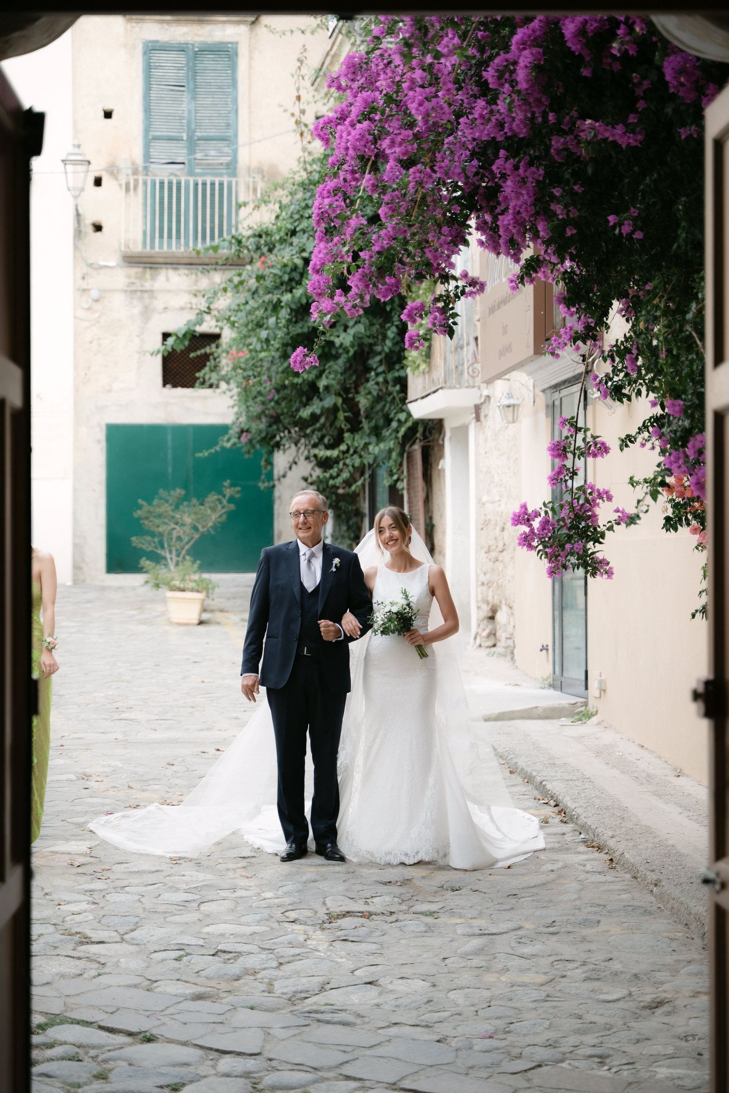 Bride and her father arriving at the ceremony beneath bougainvillea