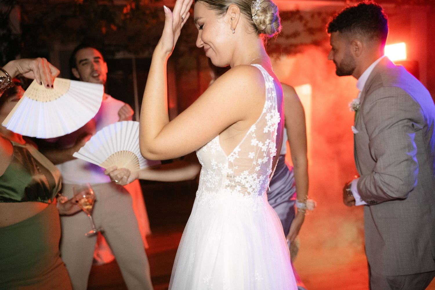Bride dancing with friends beneath red party lights