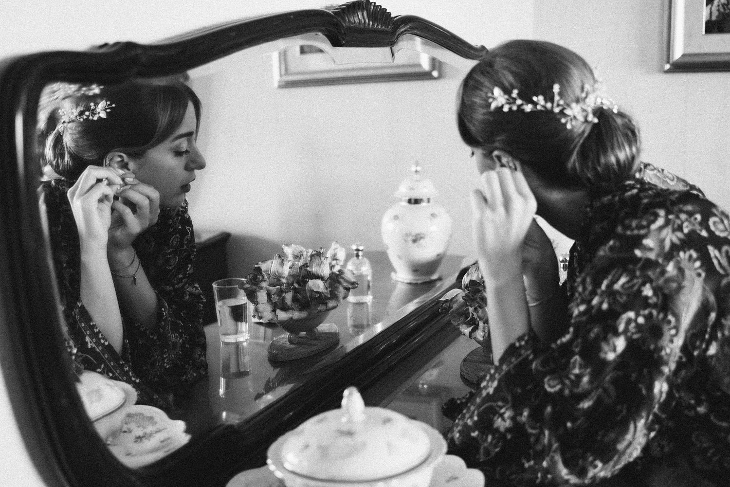 Bride putting on her earrings reflected in a mirror