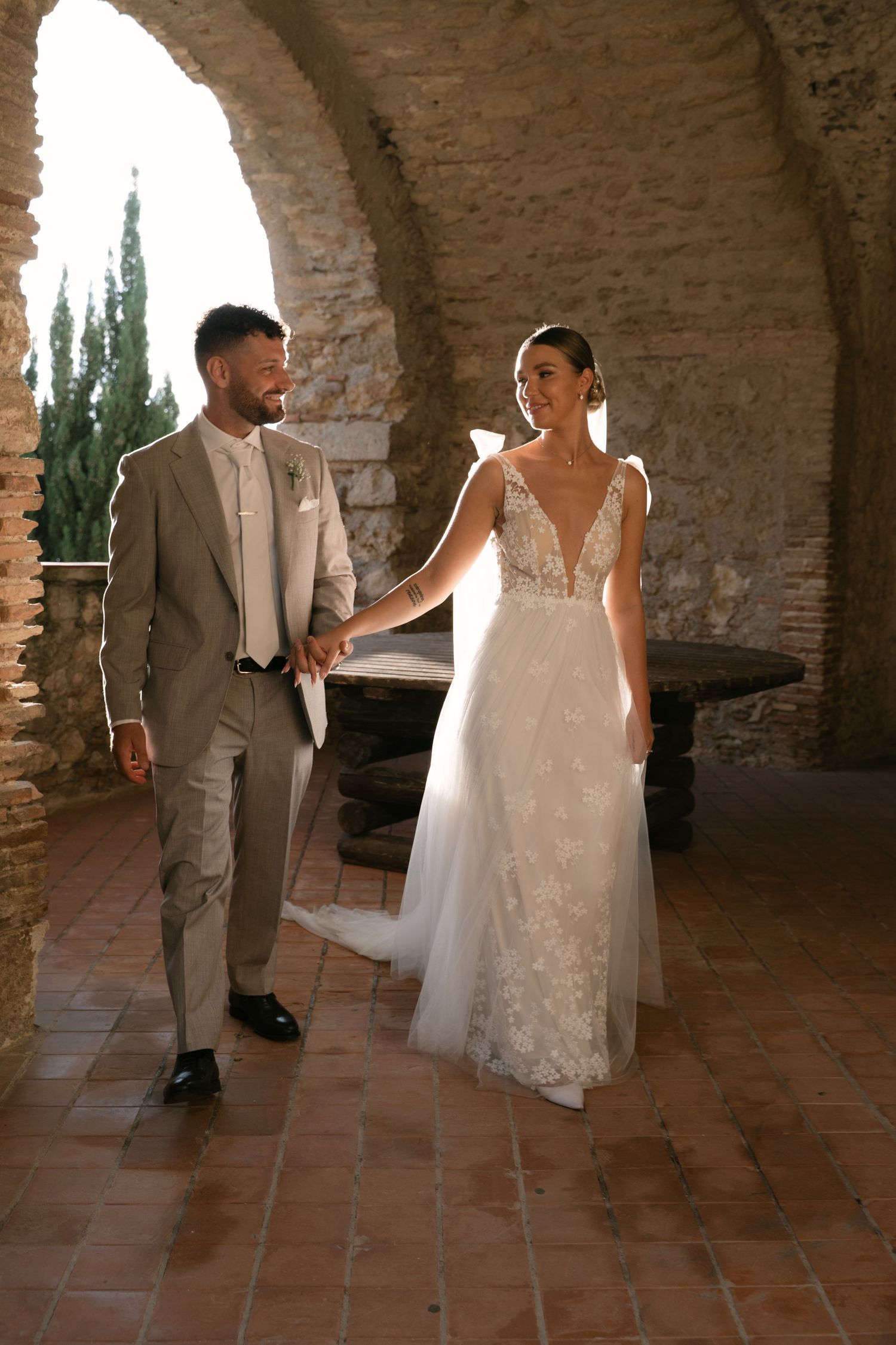 Bride and groom beneath a historic stone arch during golden hour