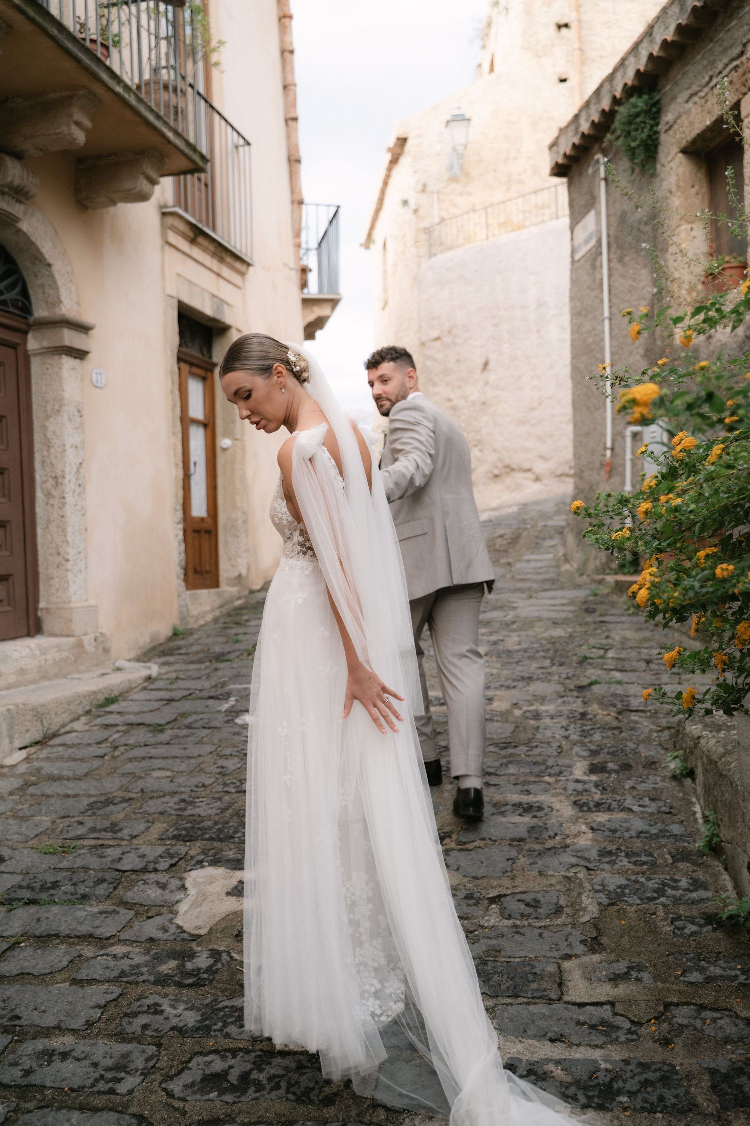 Bride leading the groom through a narrow cobblestone street in Sicily