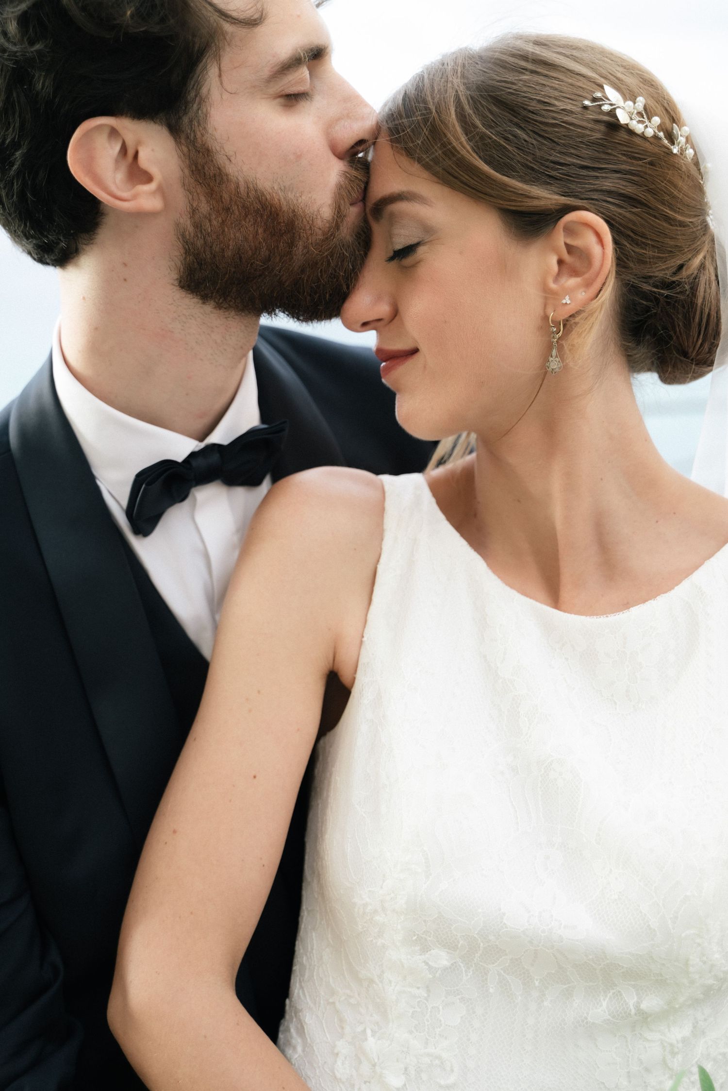 Groom kissing the bride on the forehead overlooking the sea