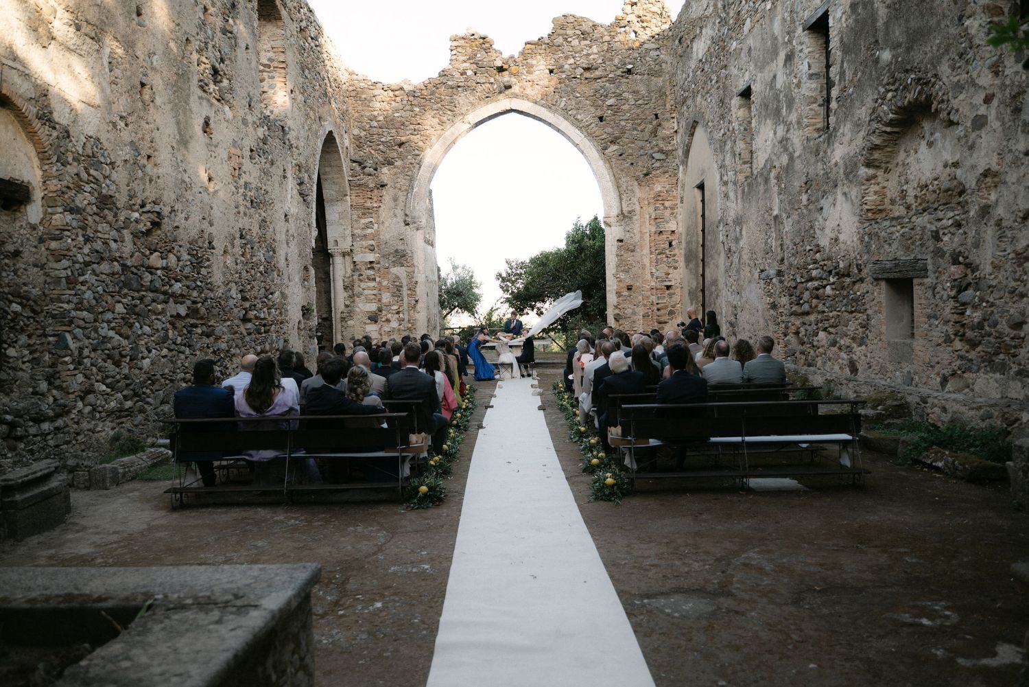 Wide view of the wedding ceremony beneath the ancient stone arch