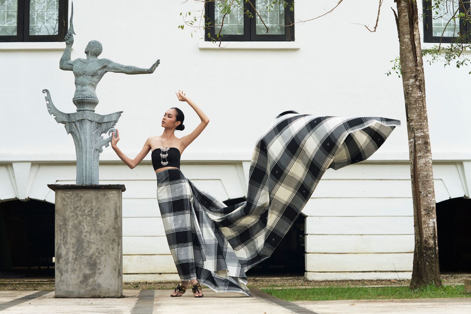 Model in flowing black and white plaid gown posing near outdoor sculpture.