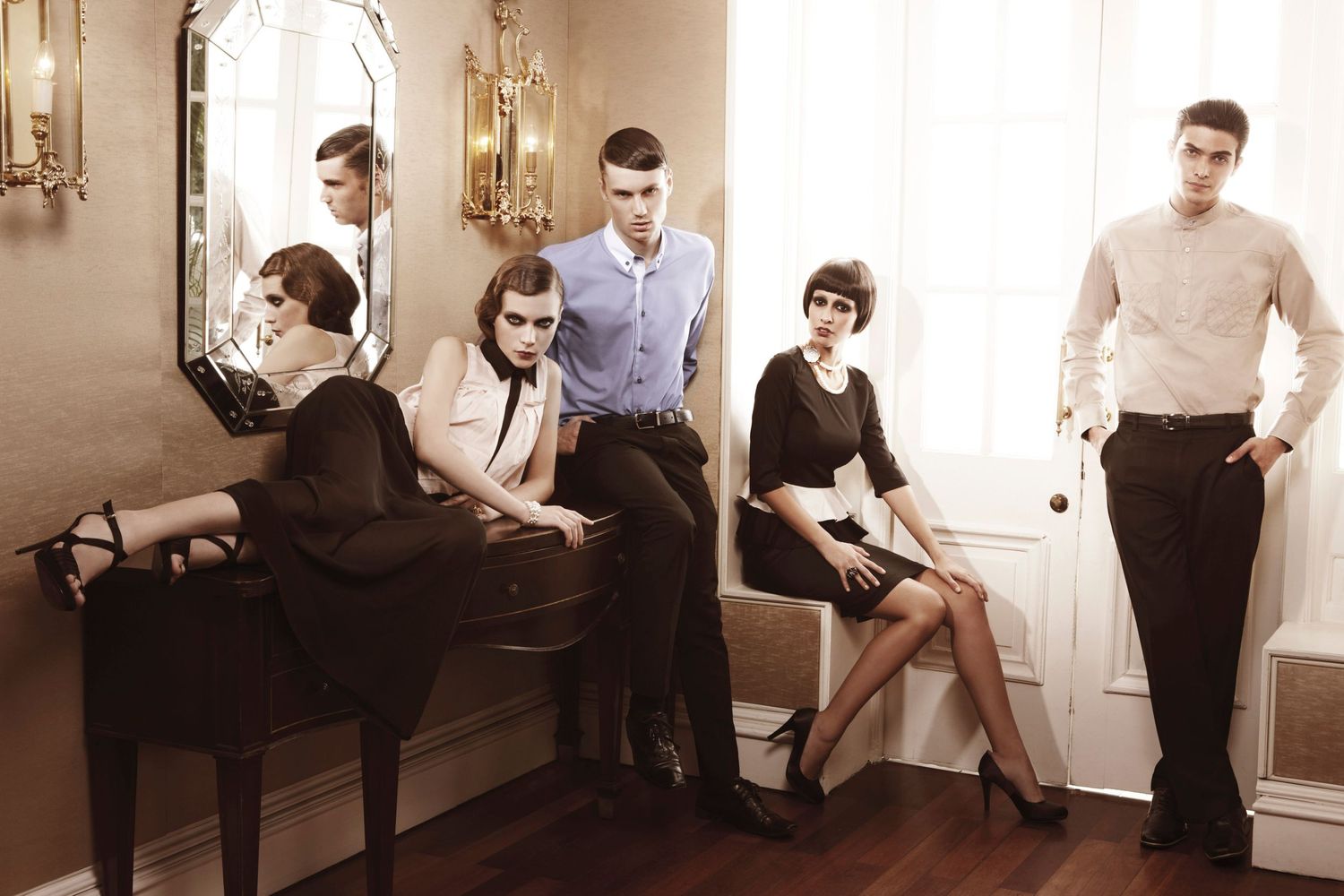 Group of elegantly dressed models pose in vintage-inspired black and white outfits in classic interior setting.