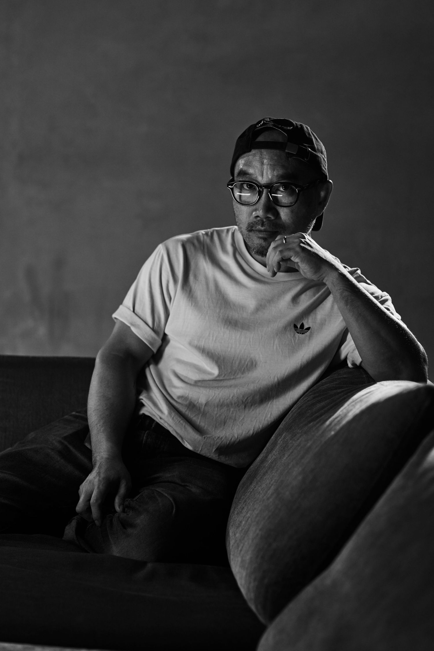 Middle-aged man in white t-shirt sits thoughtfully on sofa in black and white portrait.