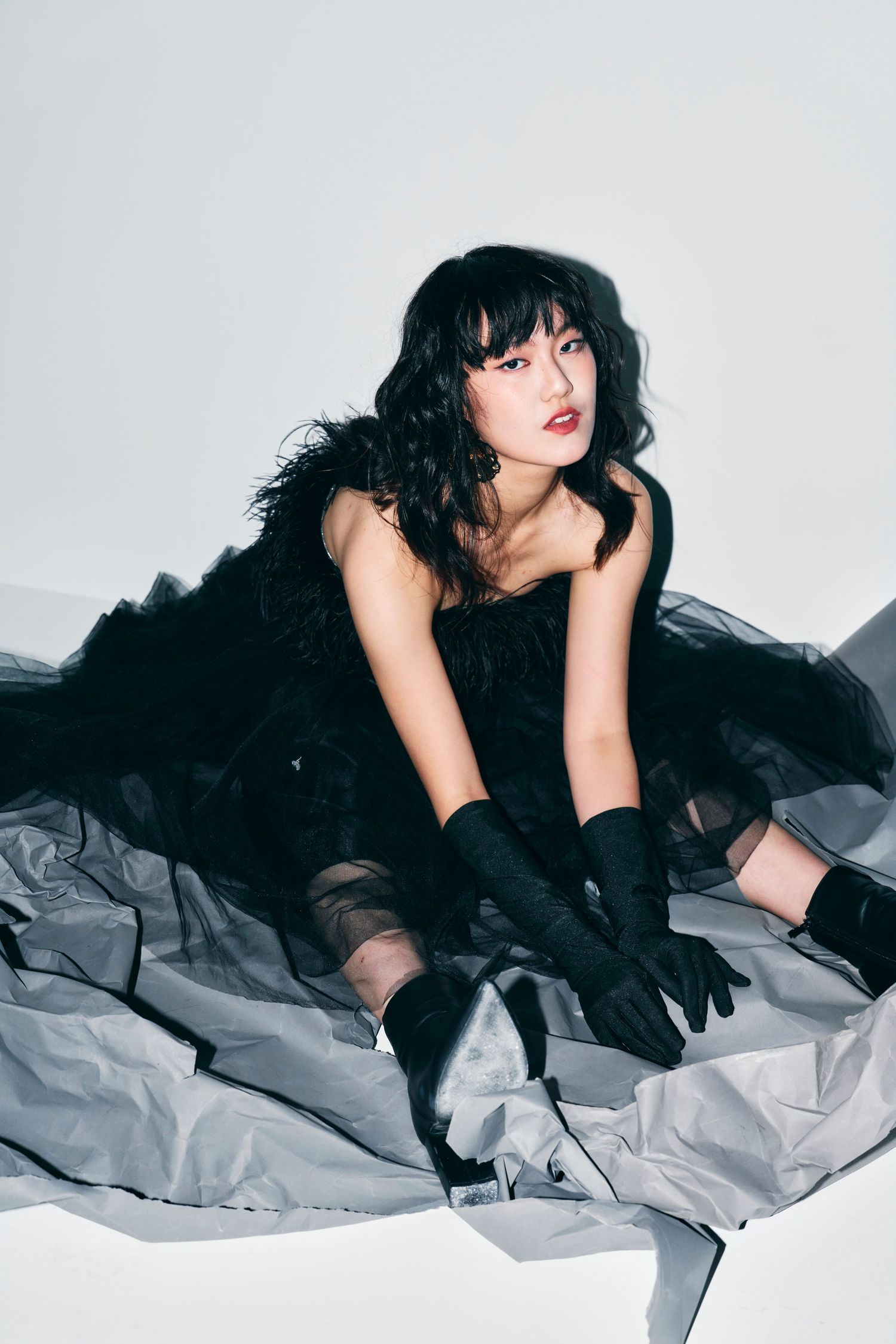 Young woman in black feathered dress and gloves poses gracefully on studio floor.