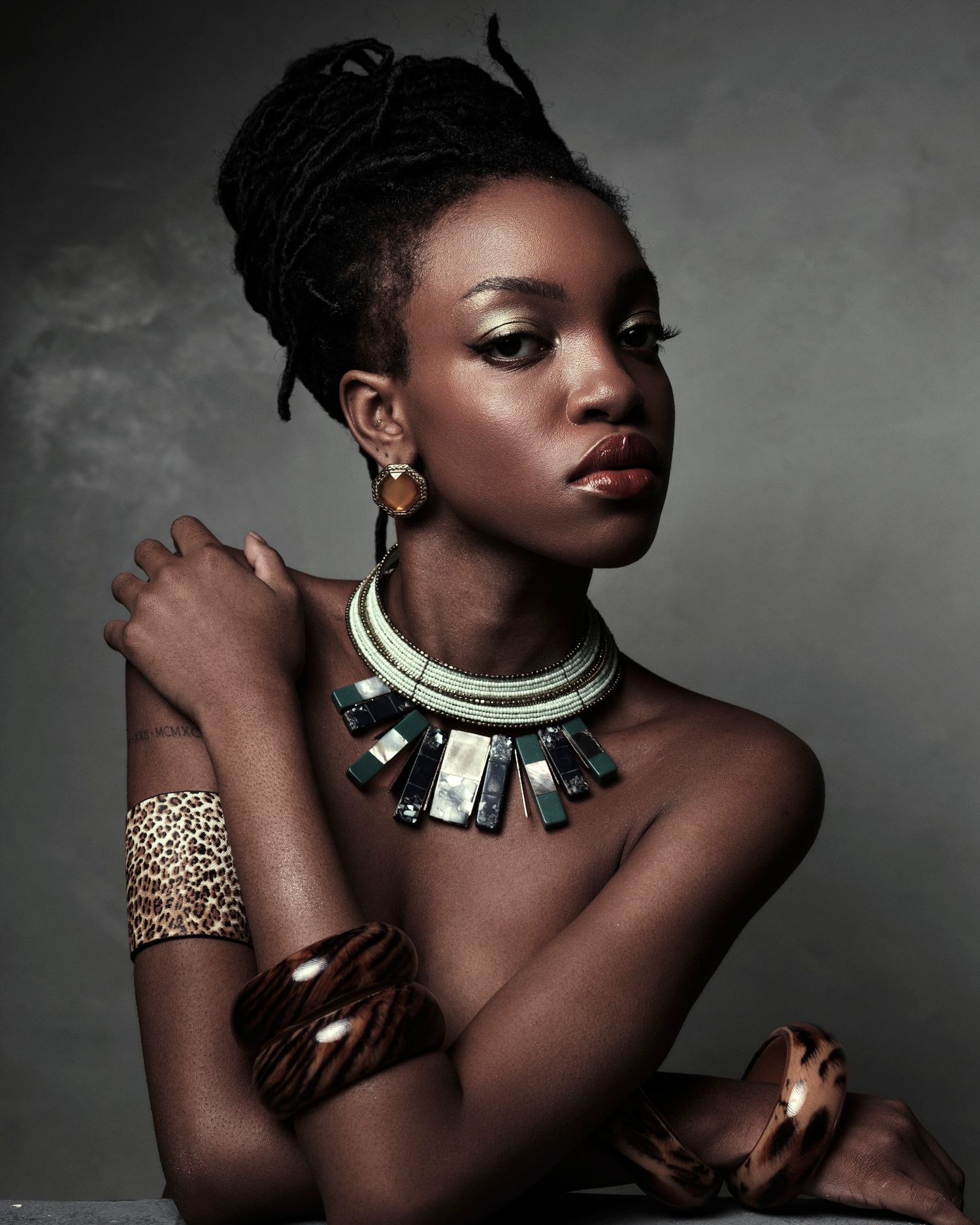 Black woman wearing bold geometric necklace with leopard print cuff and tortoise bangles against smoky background.