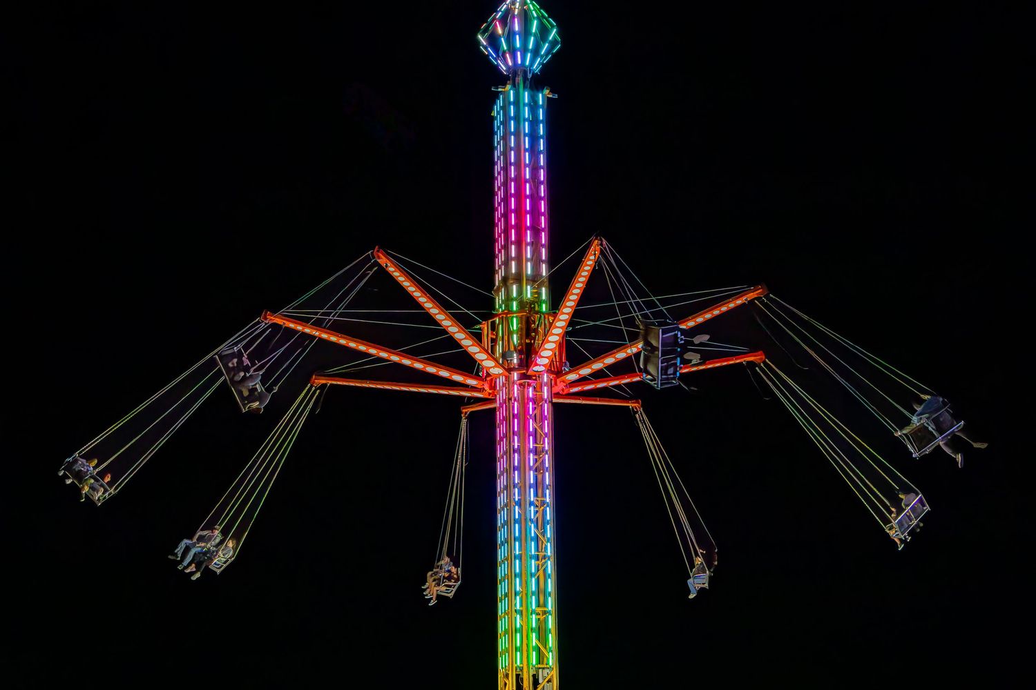 Colorful illuminated carnival swing ride glowing with rainbow LED lights against a dark night sky.