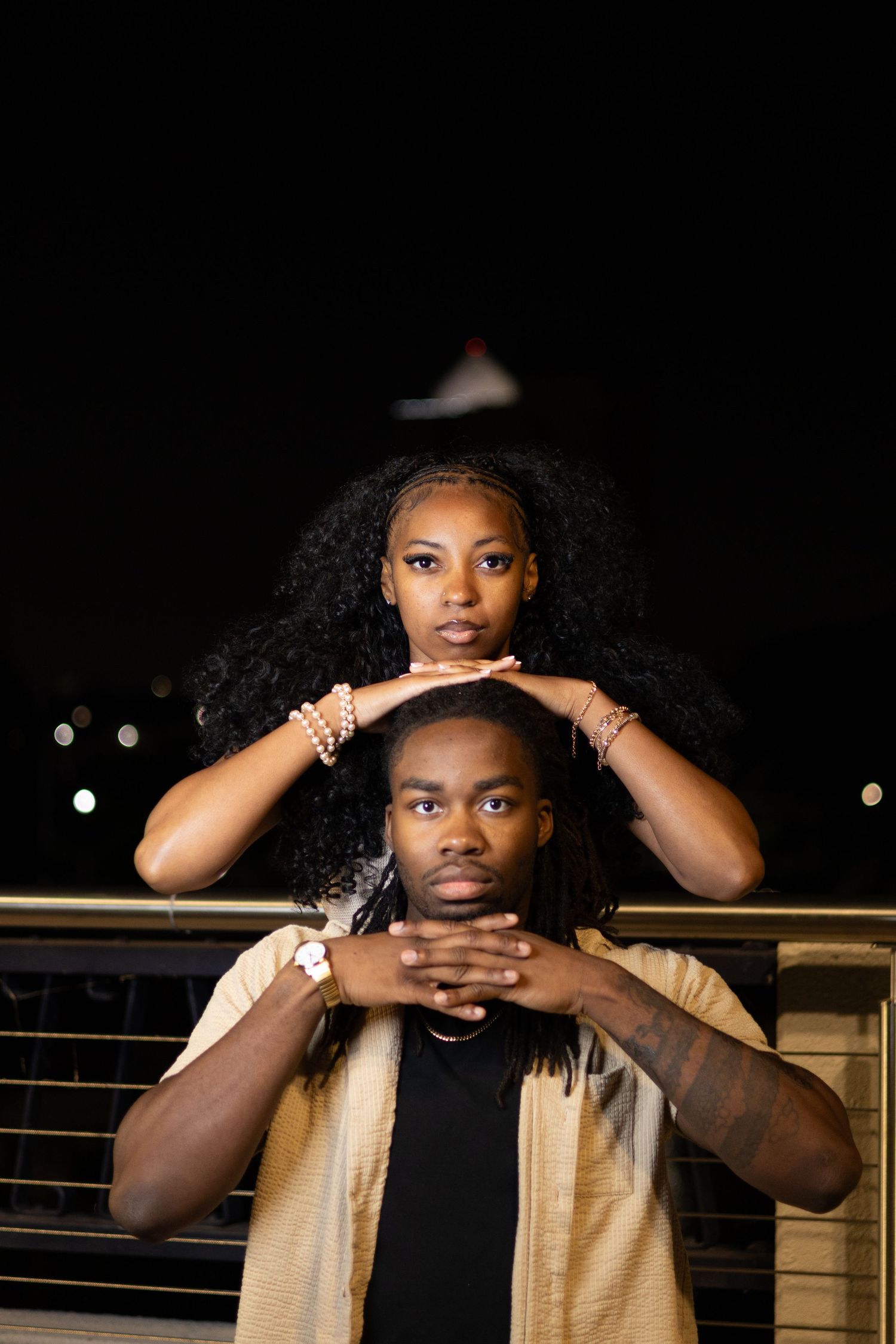 A woman rests her hands on a man's head as they pose together at night.