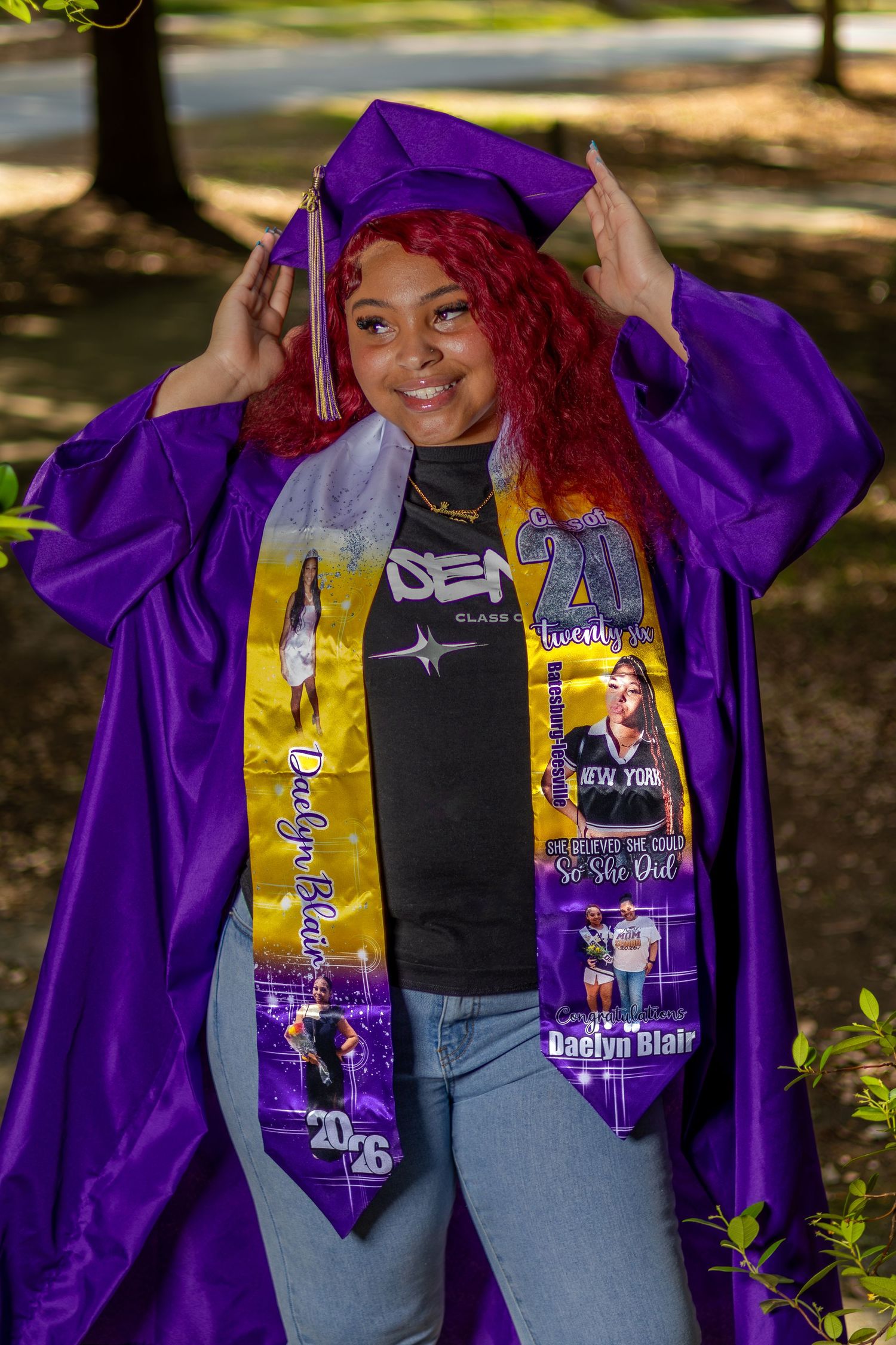 Young woman in purple graduation cap and gown with custom sashes smiling outdoors, celebrating her 2026 graduation.