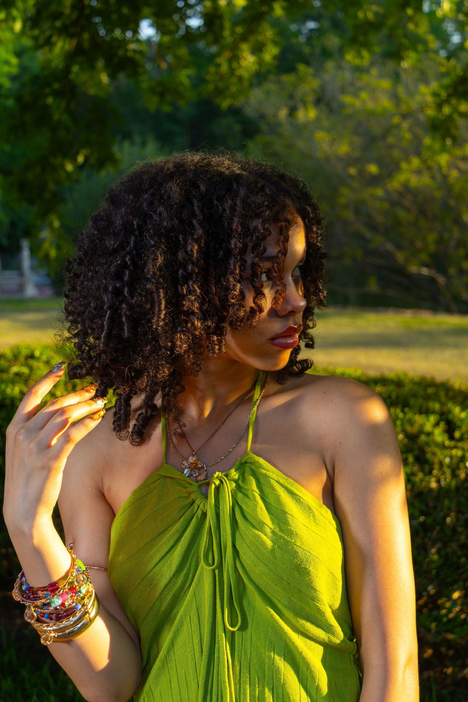 Young Black woman in green halter dress posing in sunny park.