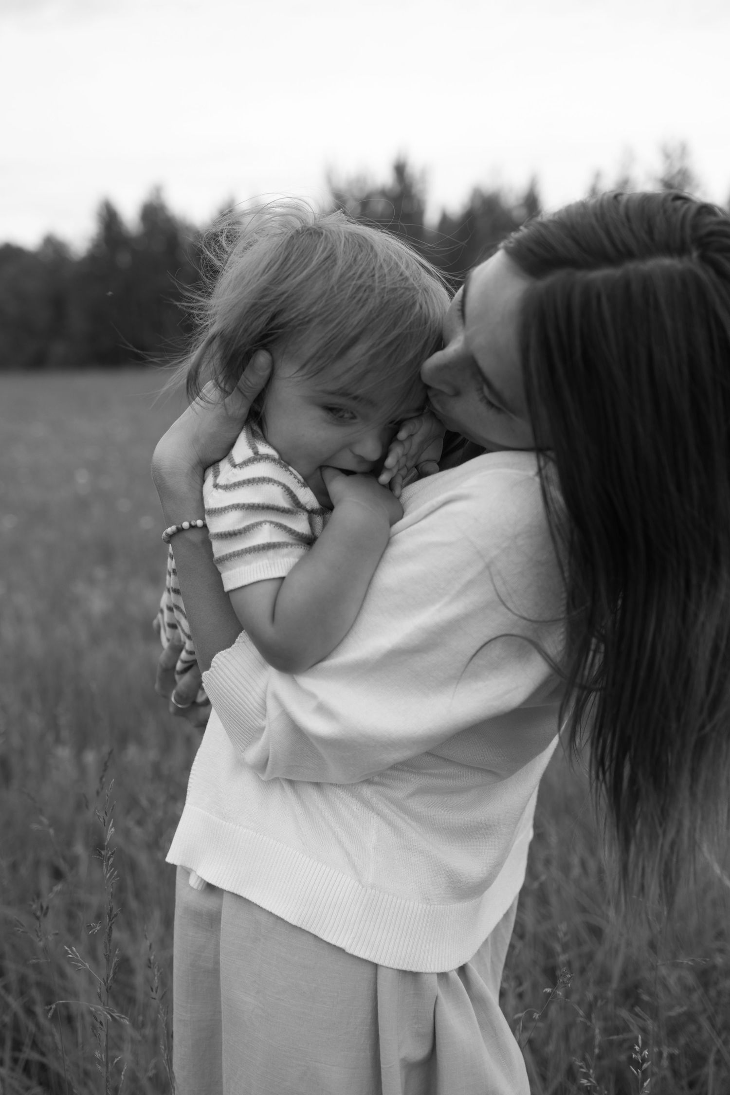 Black and white photo of a mother tenderly kissing her young child in a field. Family Photography.