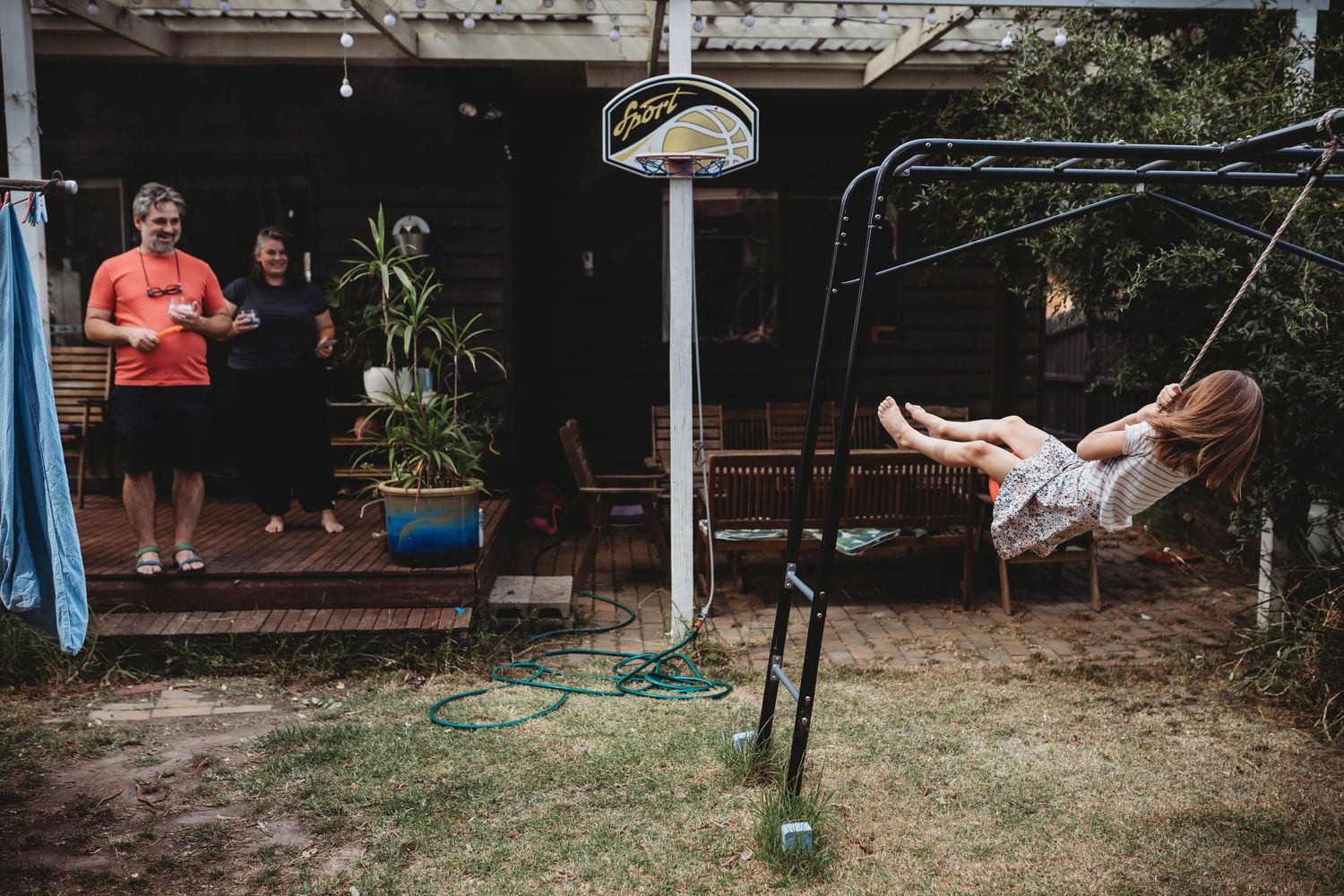 Girl swinging in backyard while family watches from home deck.