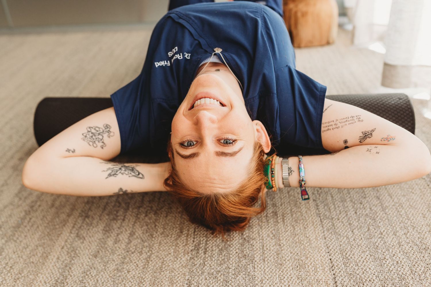 Woman with tattoos lying on floor smiling upside down in casual blue t-shirt.