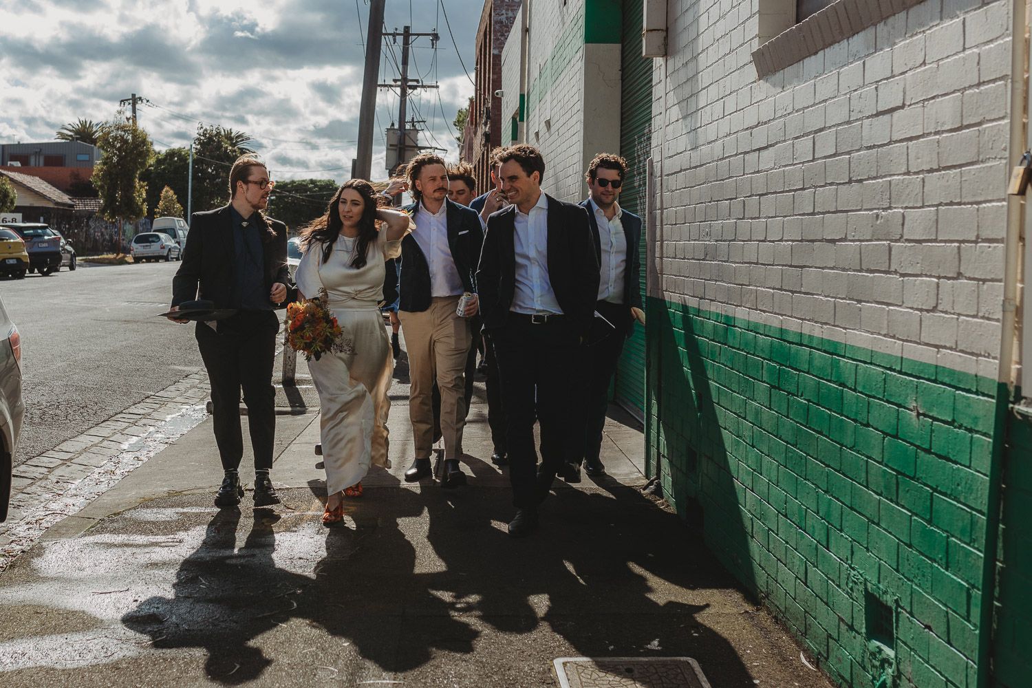 Group of well-dressed friends walking together on a city street beside a tiled wall.