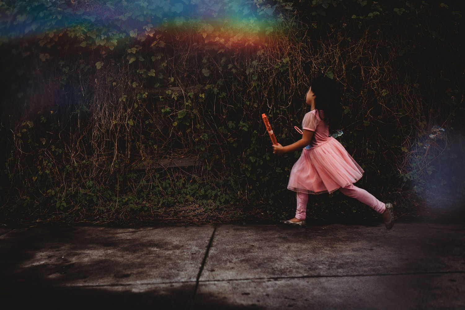 A young girl in a pink tutu dress runs along a path with a rainbow in the background.