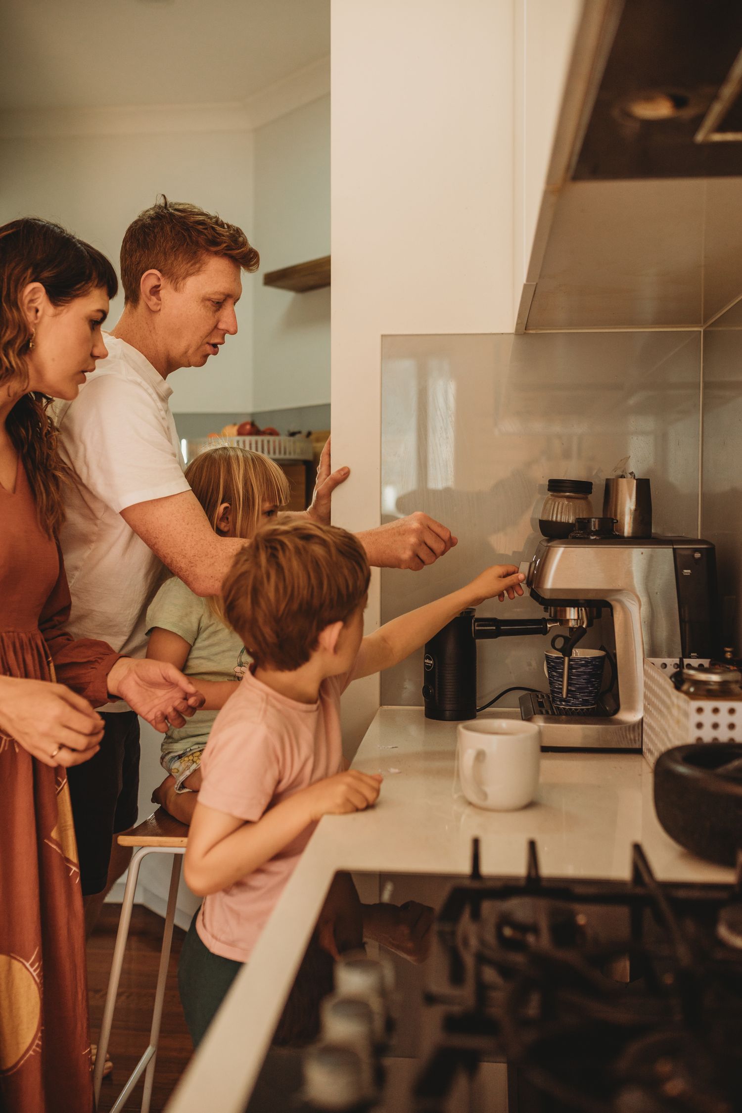 Family gathered around a coffee machine in a modern kitchen, with children helping parents make coffee at home.