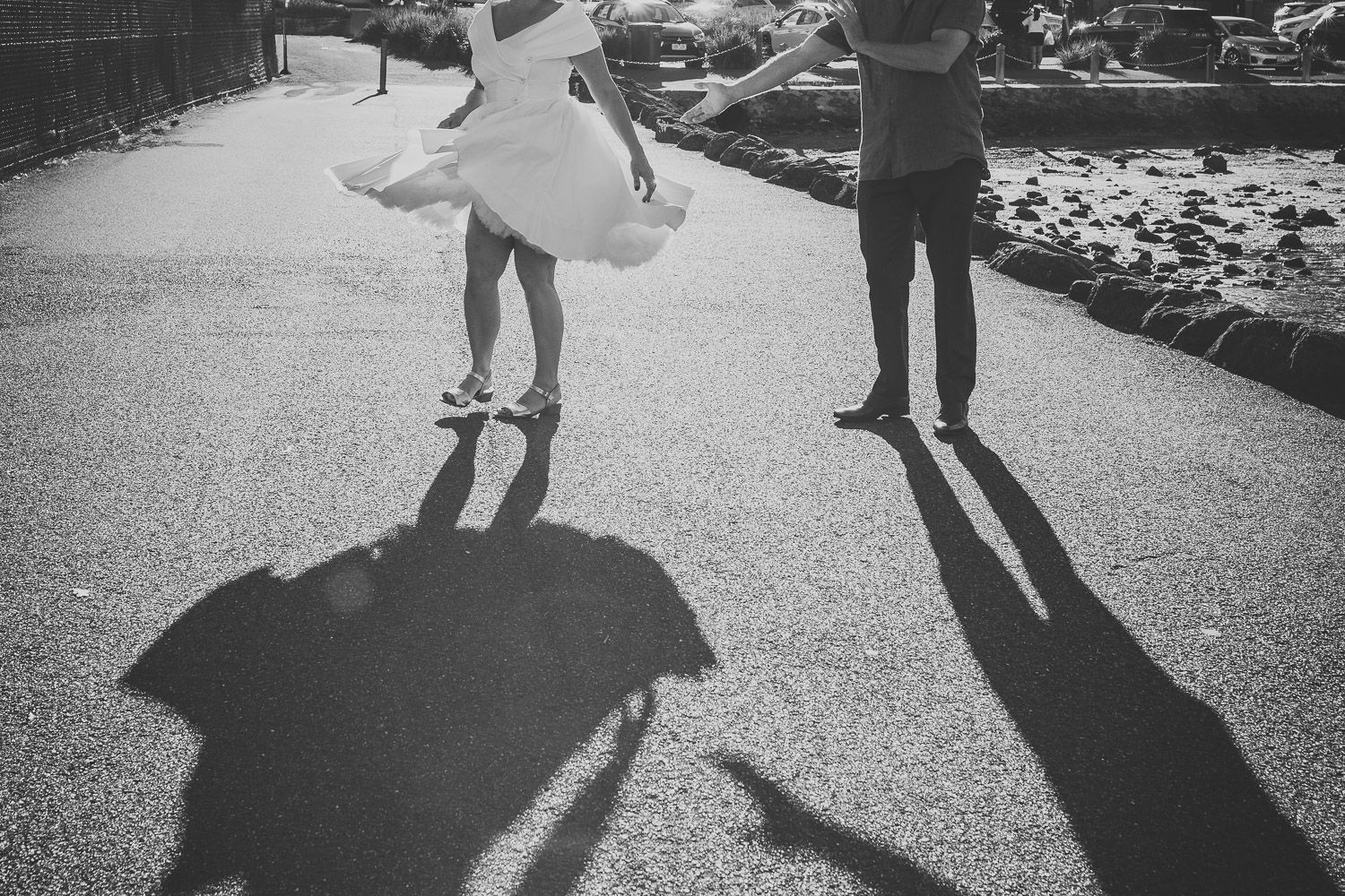 Black and white photo of bride twirling in white dress casting dramatic shadows on pavement.
