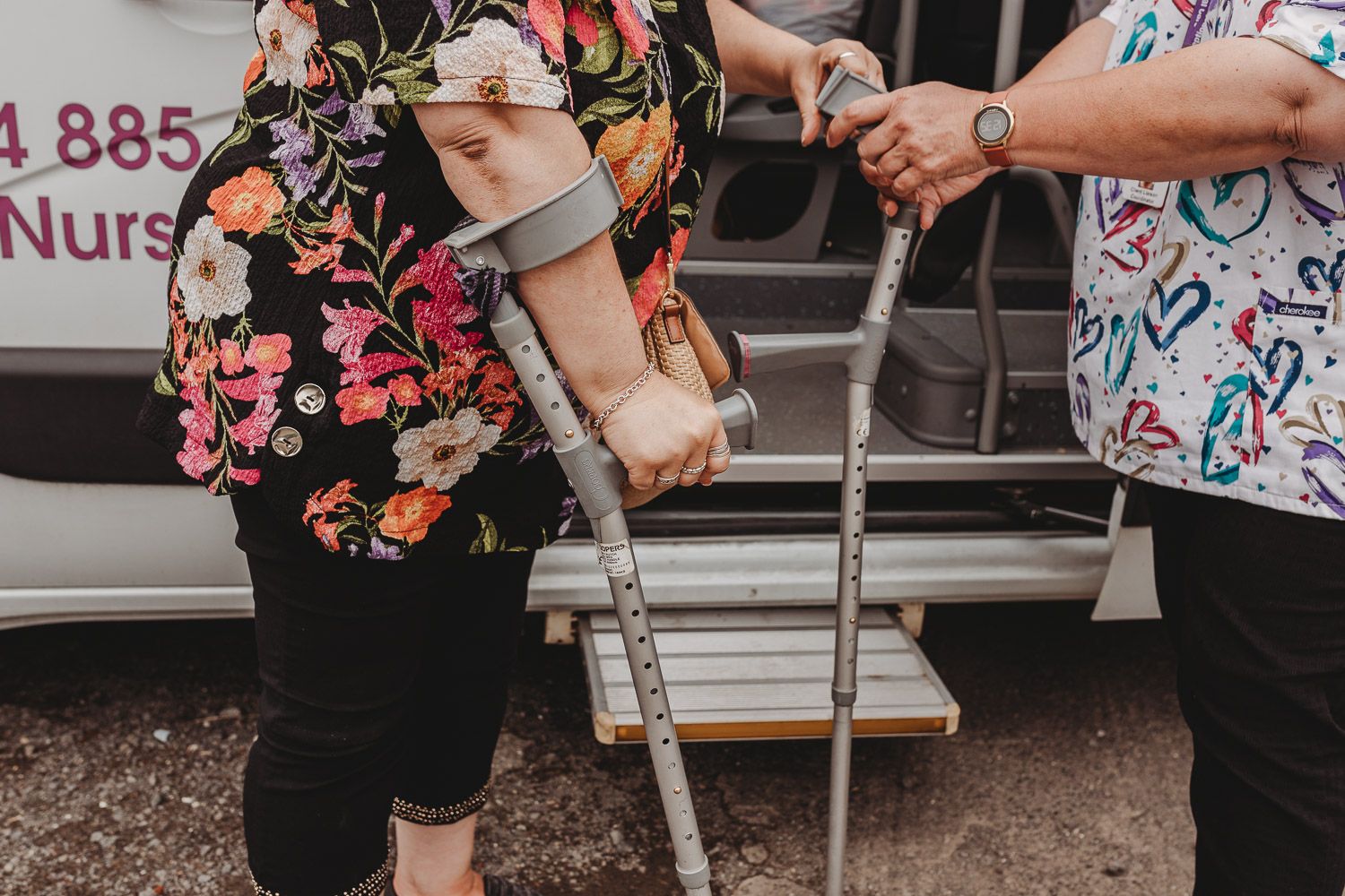 Person using forearm crutches being assisted near a medical transport van outdoors.