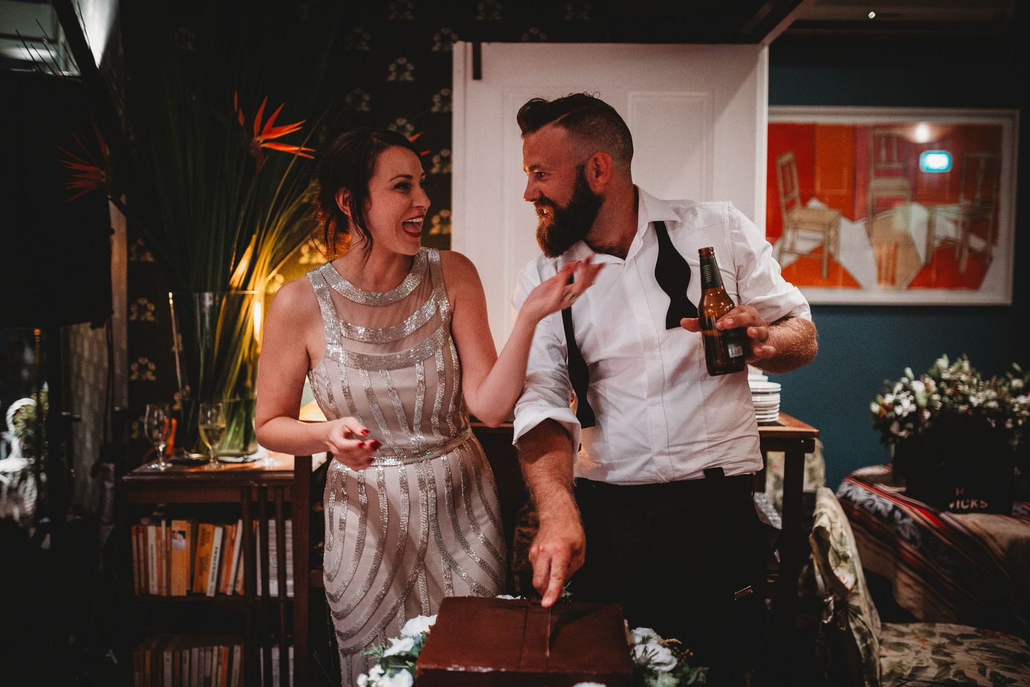 A bride and groom laughing together in a cozy, eclectic decorated reception venue.