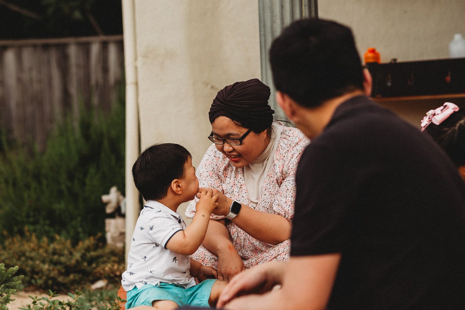 Mother in hijab interacting lovingly with young toddler son in outdoor backyard setting.