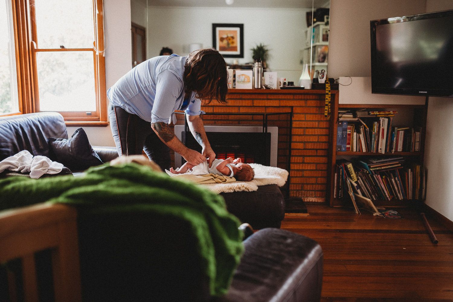 Parent changing newborn baby on table in cozy living room with brick fireplace.