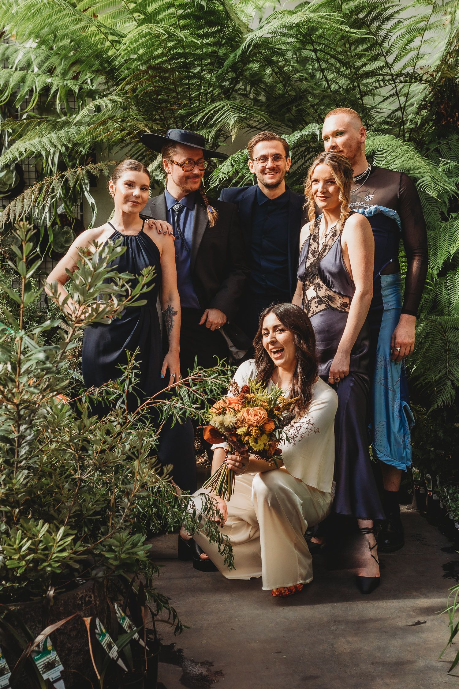 A wedding party posing together surrounded by lush tropical ferns and greenery.
