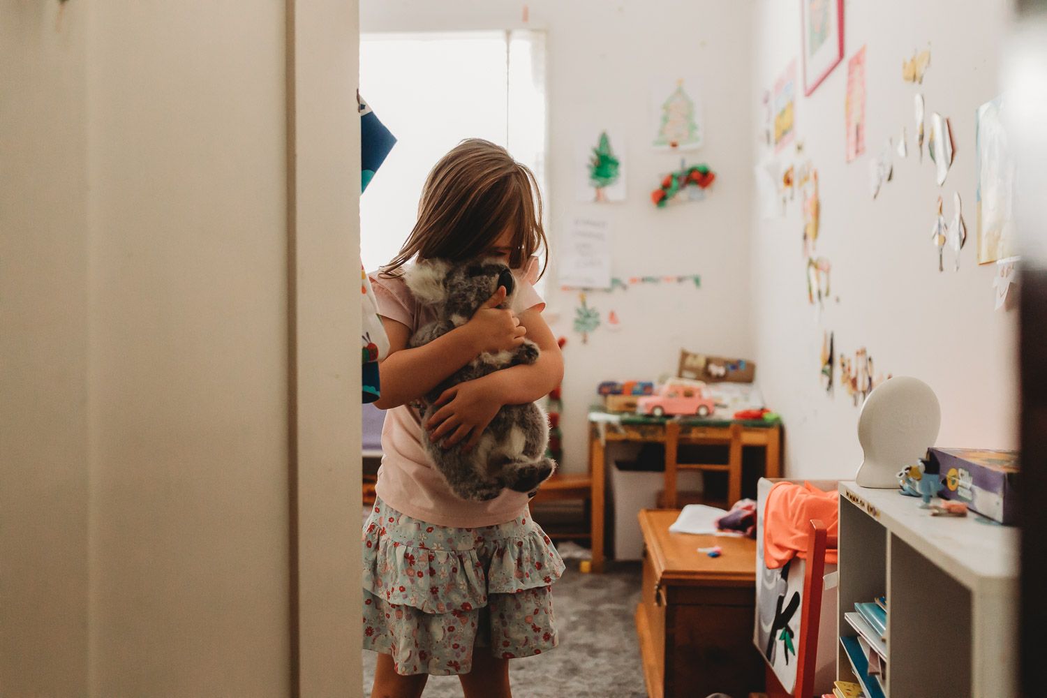 Young girl holding a cat in a colorful decorated bedroom viewed through a doorway.