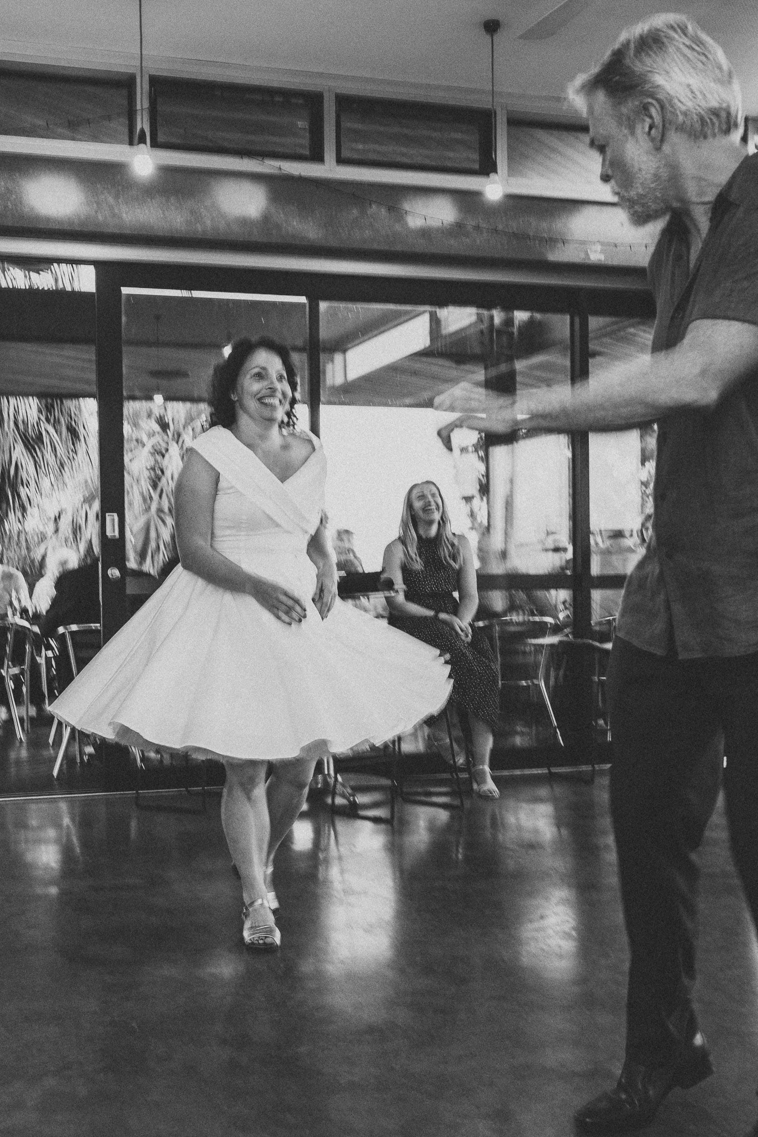 Bride spinning in white dress on dance floor as guests watch at wedding reception.