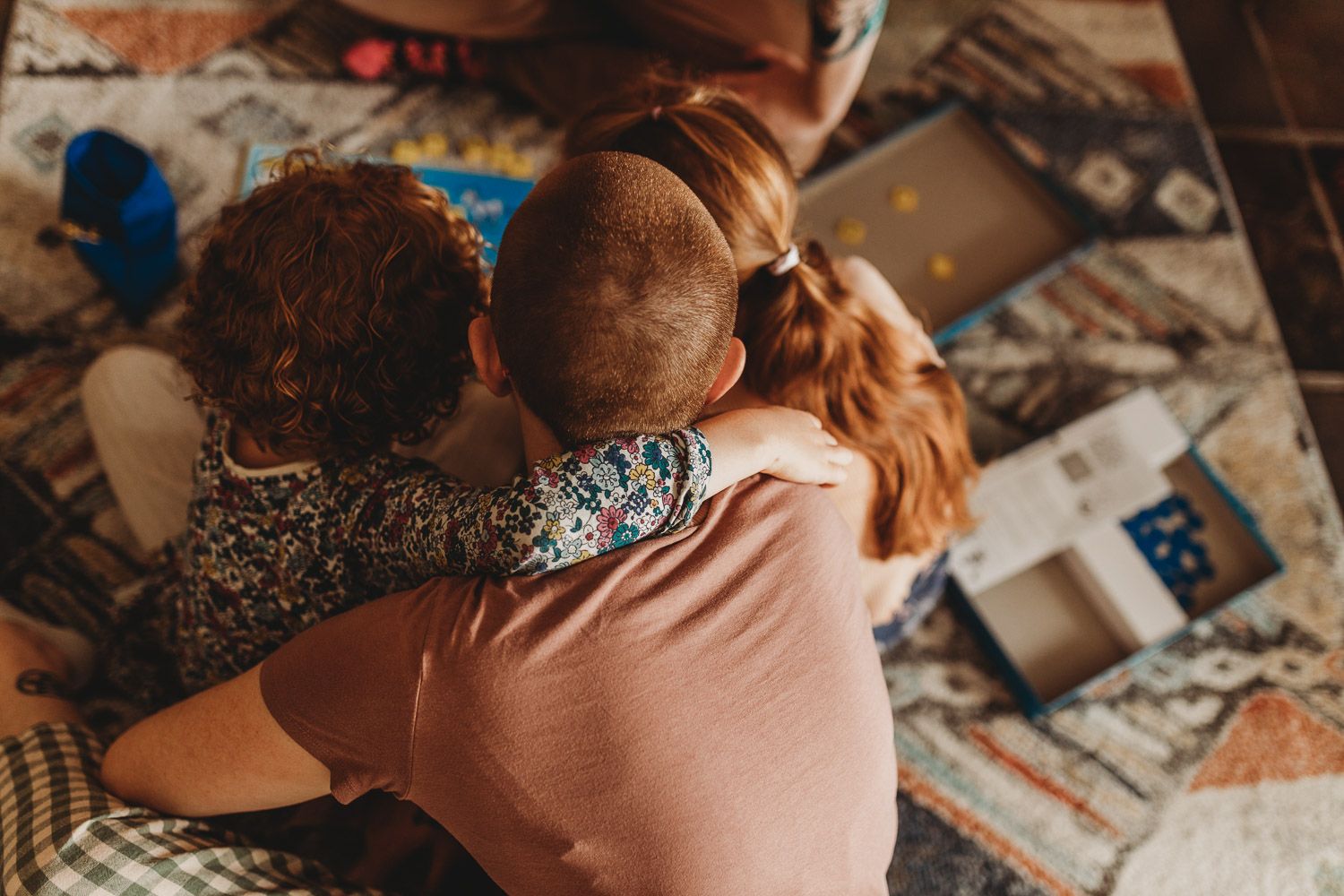 Two young red-haired siblings sharing a warm hug while sitting on a patterned rug.