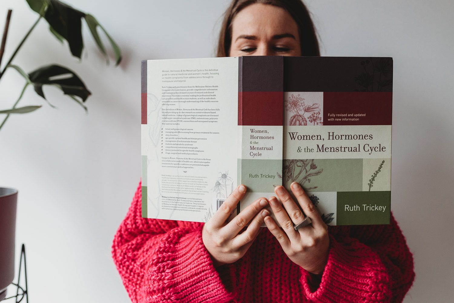 Woman in red sweater reading Women, Hormones and the Menstrual Cycle book by Ruth Trickey.