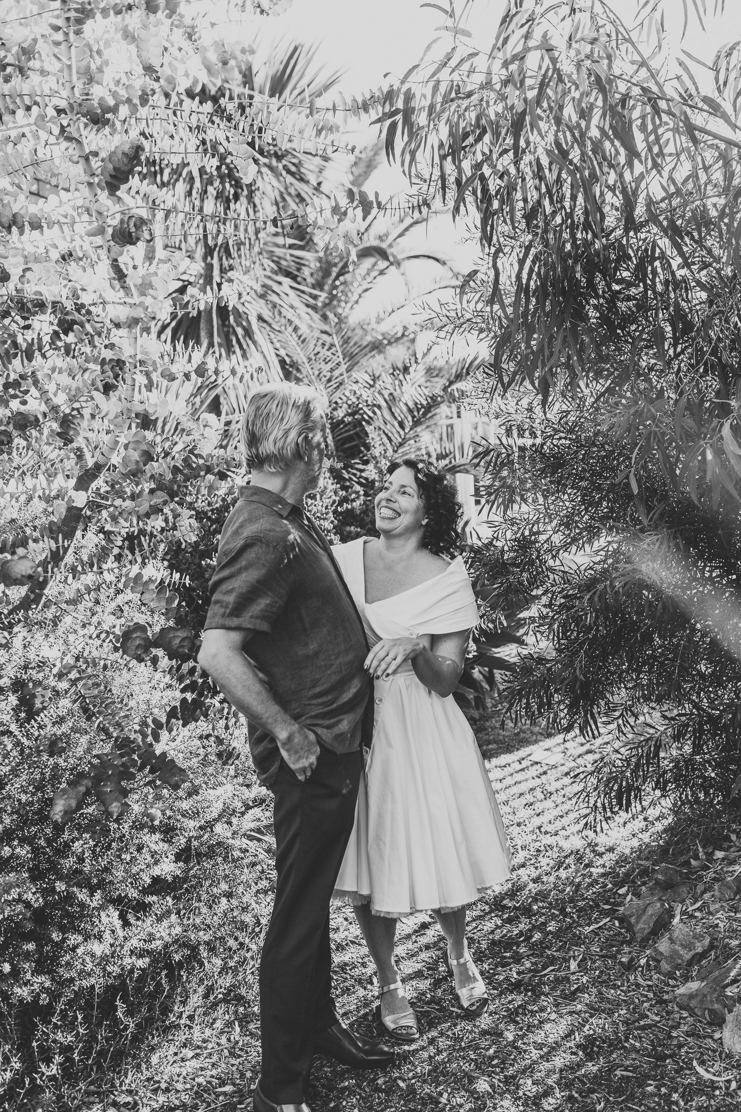 Black and white portrait of a bride and groom laughing together in a lush garden setting.