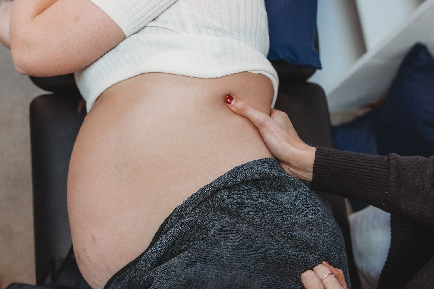 A healthcare professional examines a pregnant woman's bare belly during a prenatal checkup appointment.