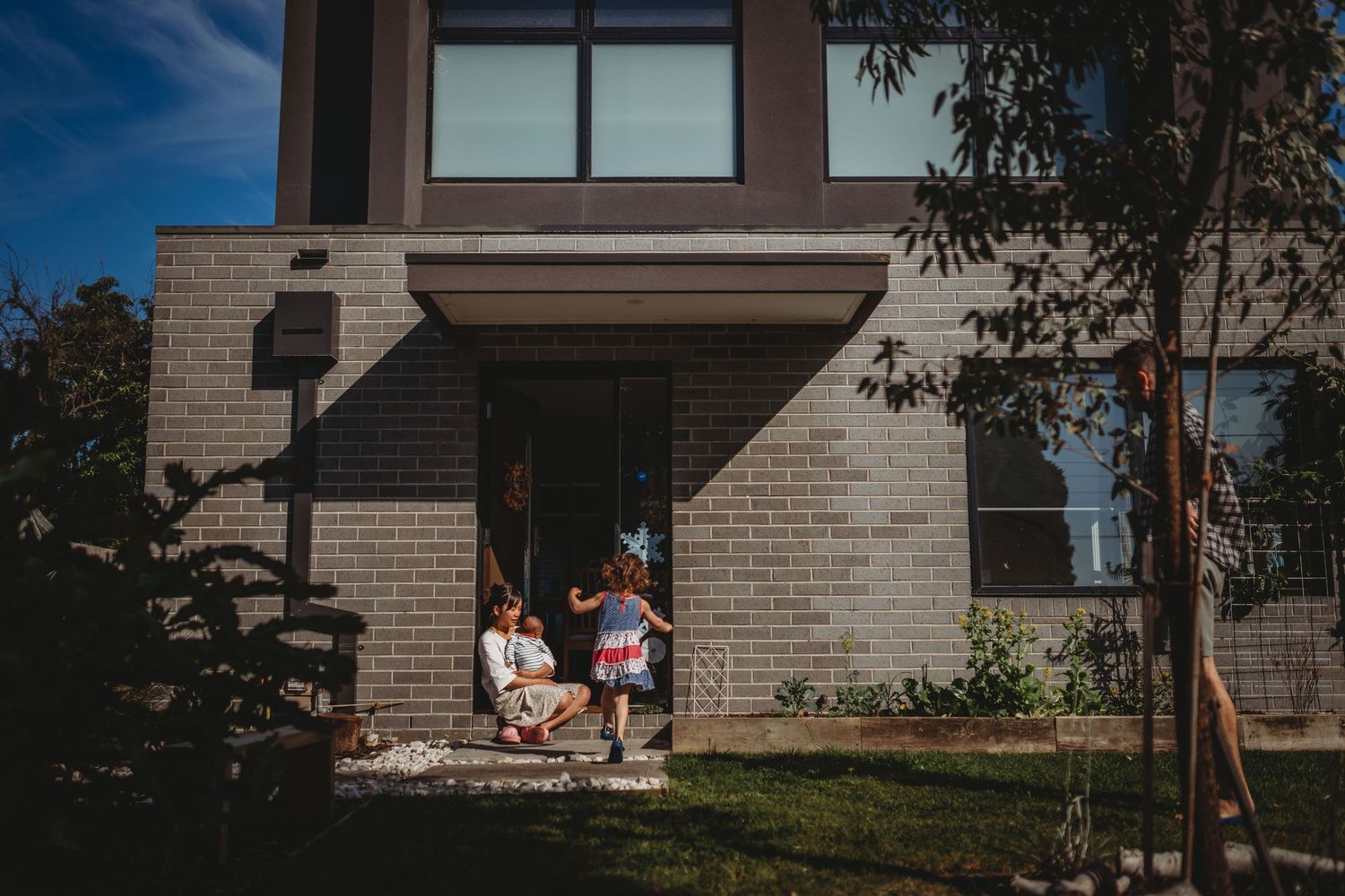 Family relaxing on modern brick home front steps on sunny day.