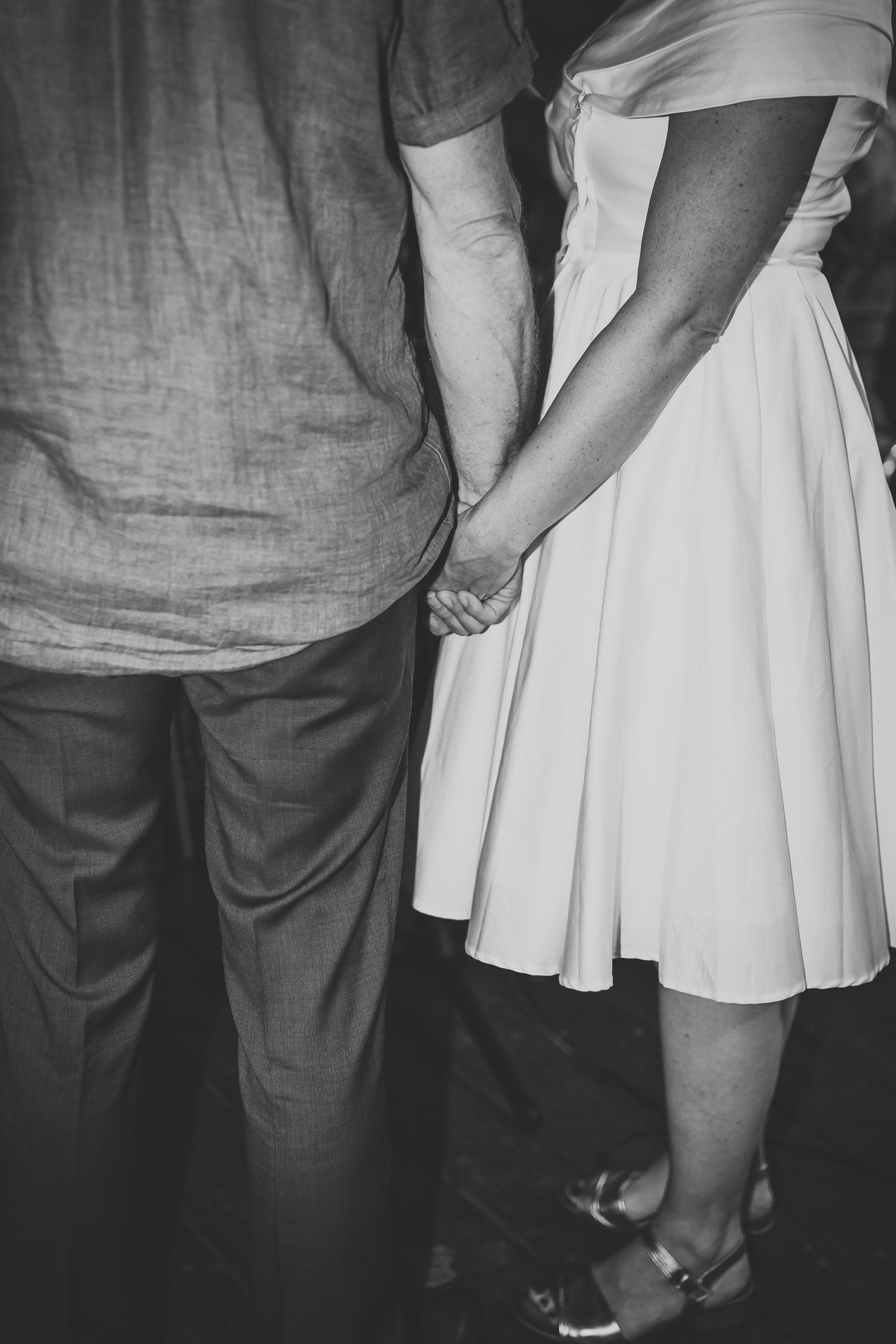 Black and white close-up of bride and groom holding hands at wedding ceremony.