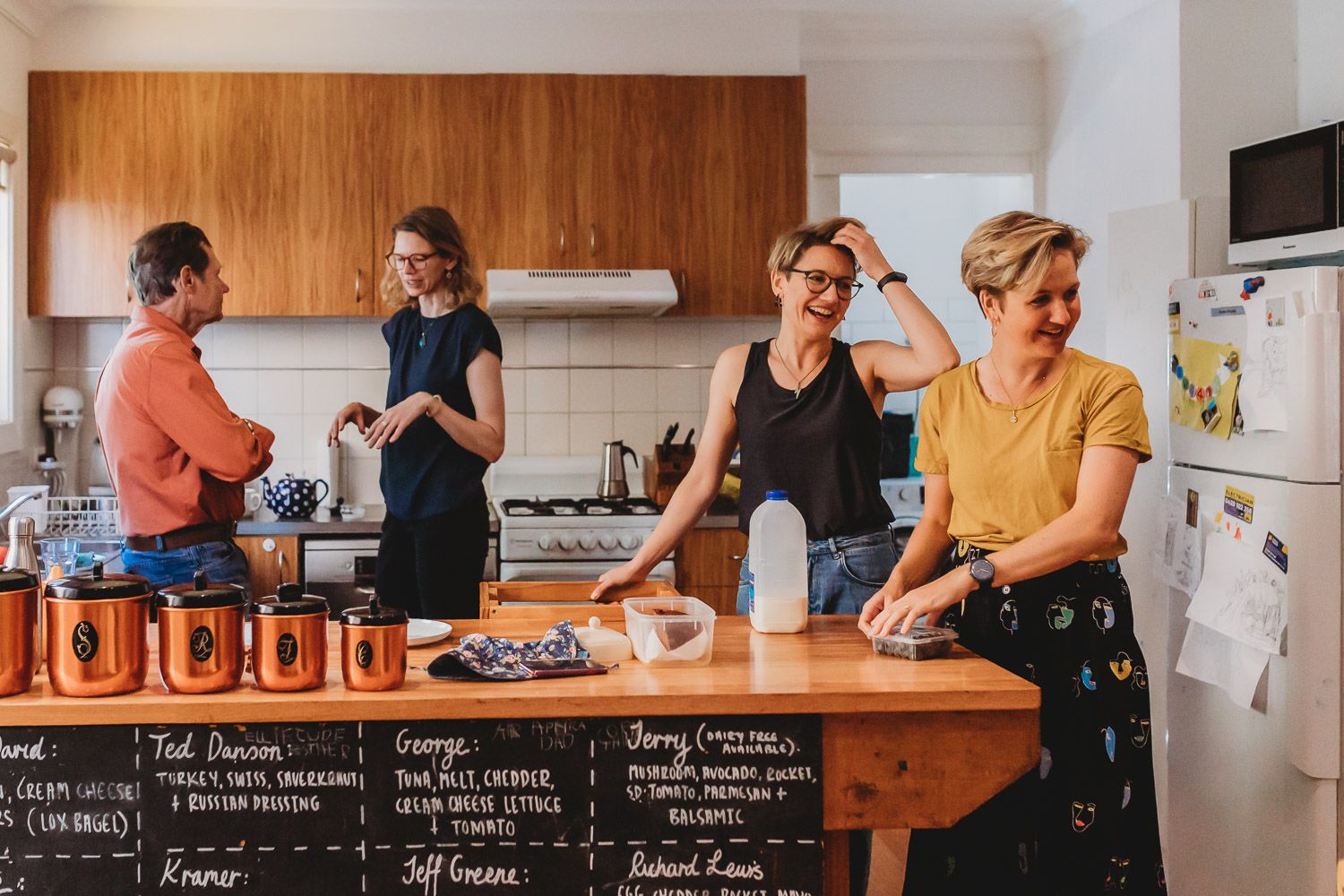 Four women gathered around a kitchen island with jars and food in a home kitchen.