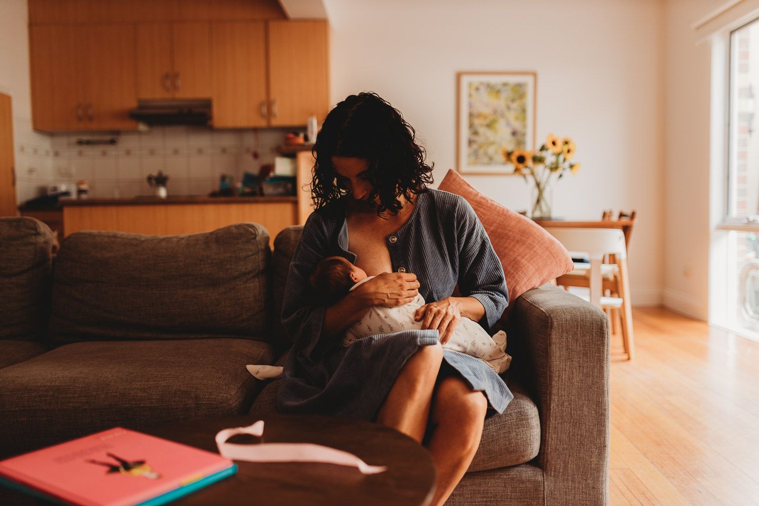 A mother breastfeeding her newborn baby while sitting on a couch in a warm, cozy living room.