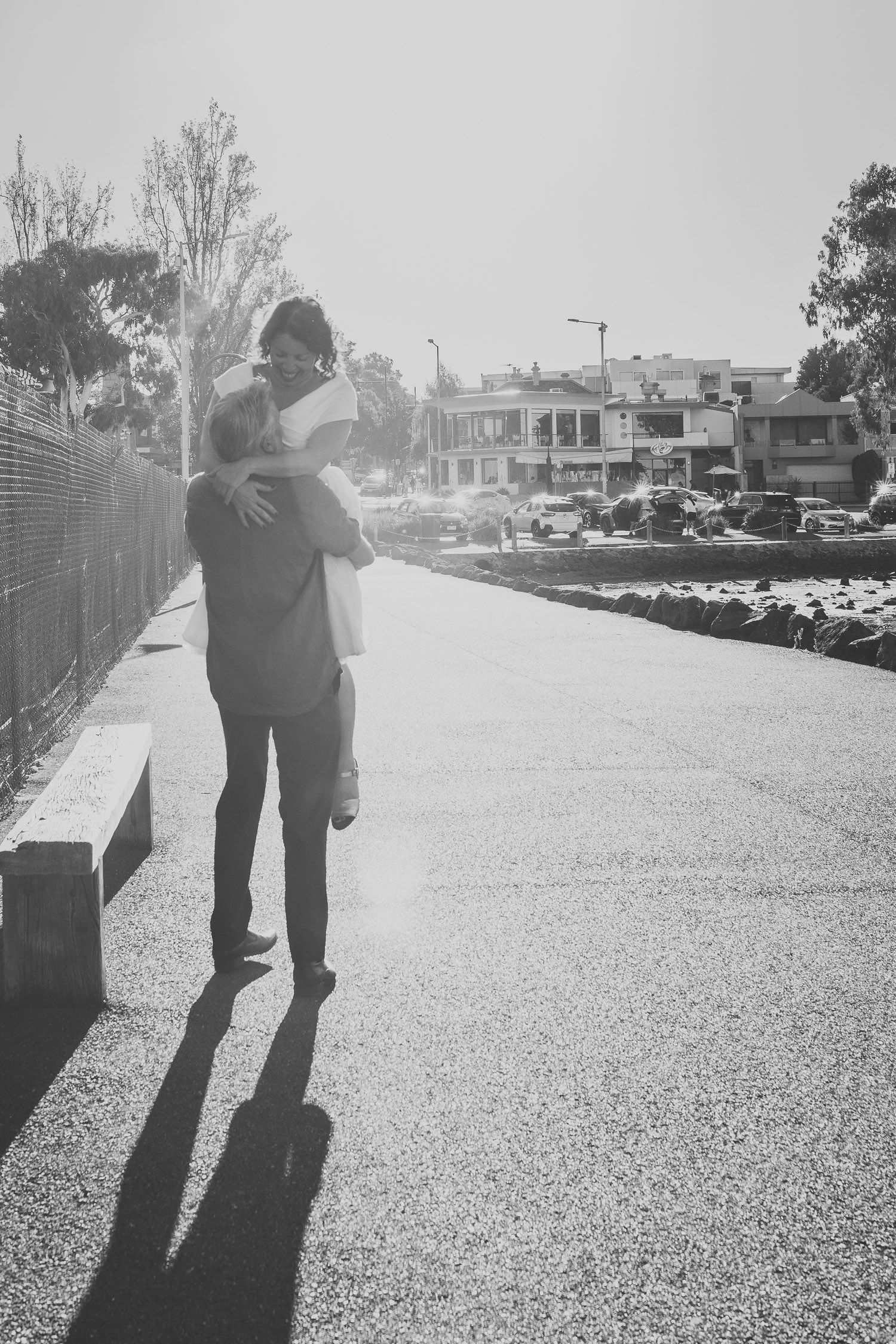 Groom carrying bride in his arms on a sunny street in a romantic black and white wedding photo.