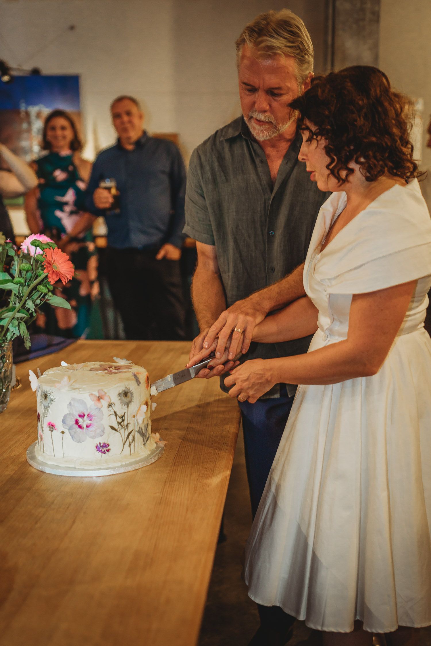 Bride and groom cutting elegant floral wedding cake together at reception table.